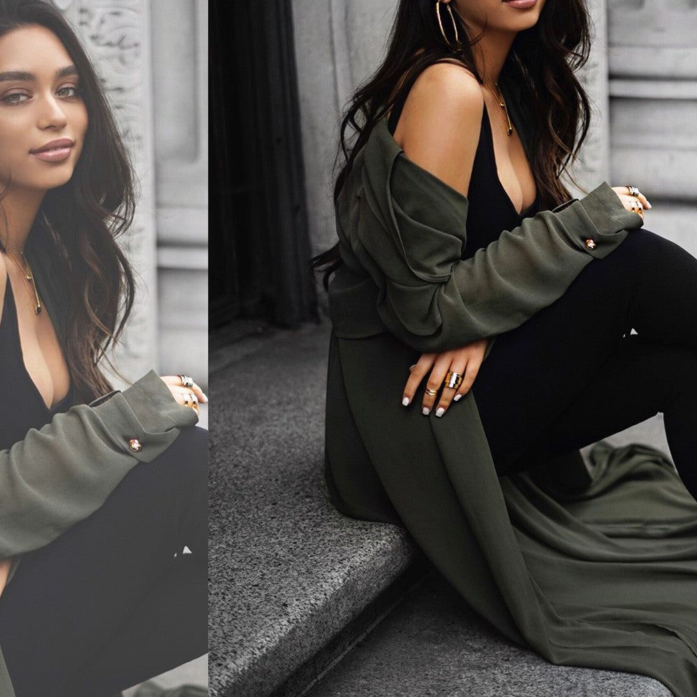 Fashion portrait of a woman in an olive green coat over a black outfit, sitting on concrete steps.