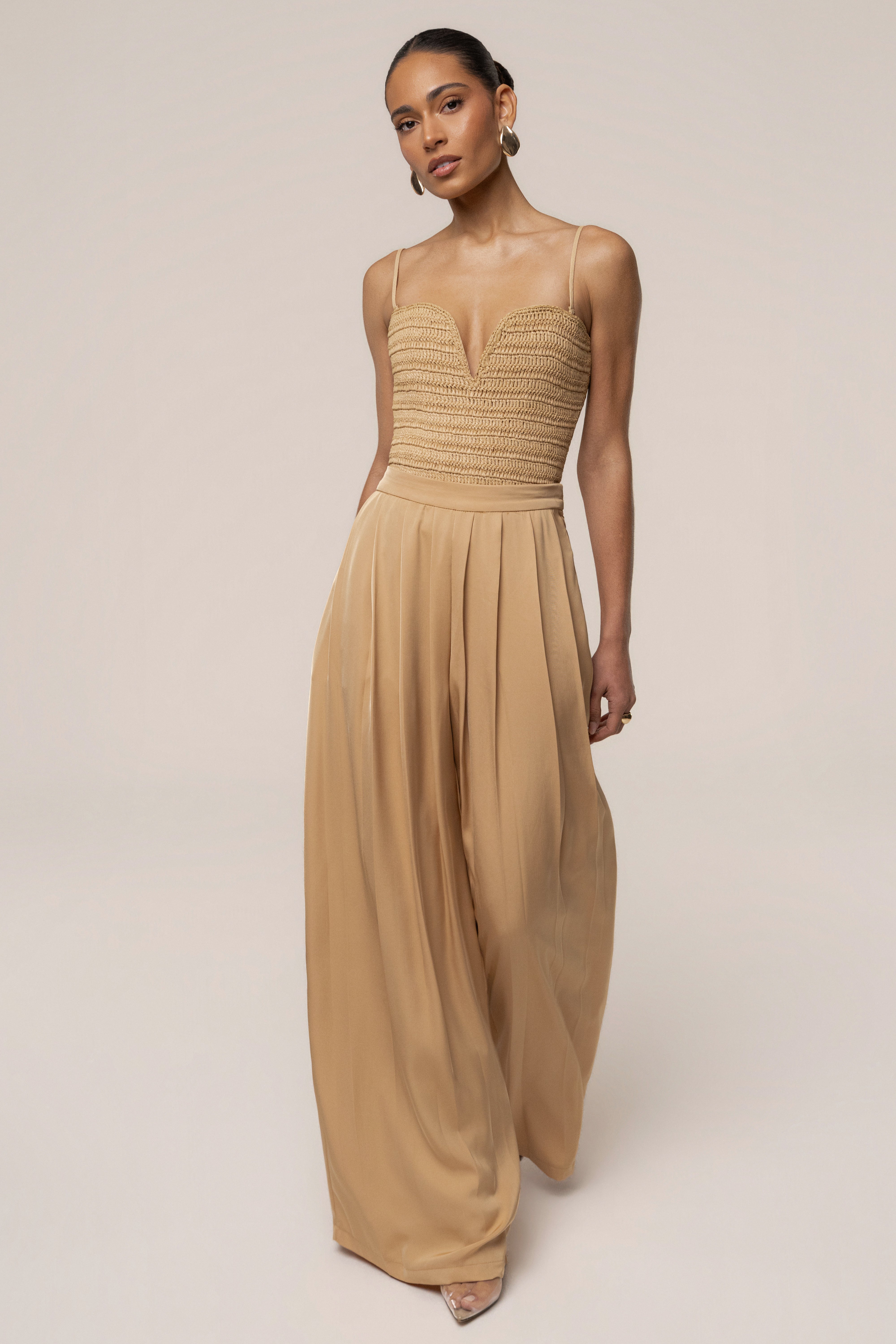 Beige Clara wide-leg pleated trousers by JLUXLABEL, shown in a natural pose, highlighting the flowy fabric and tailored fit.