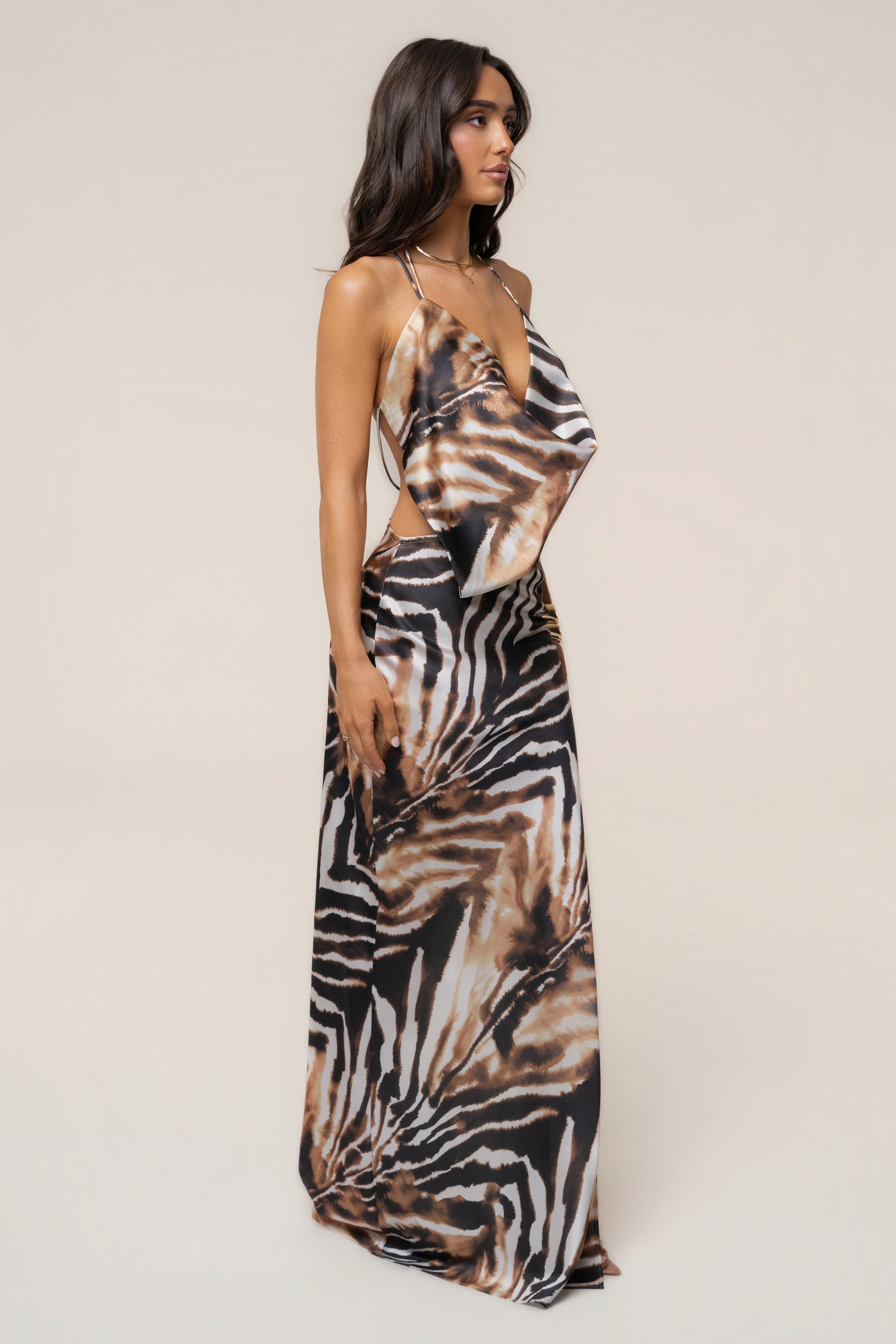 Side profile of a model in the zebra print Delmara Cowl Maxi Dress with a side waist cutout and flowing draped panel