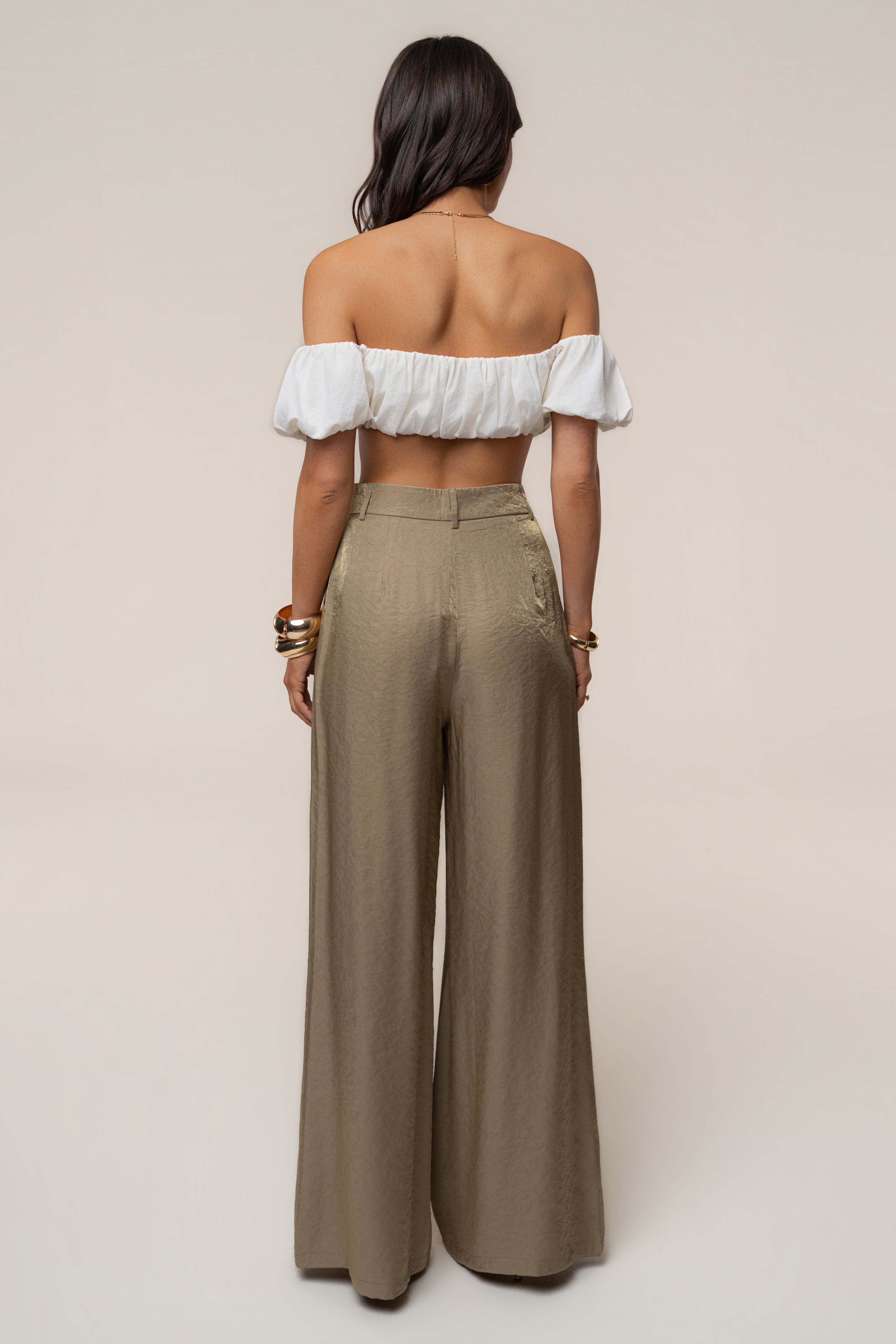 Full back view of a model in a white off the shoulder top with metallic olive wide leg pants.