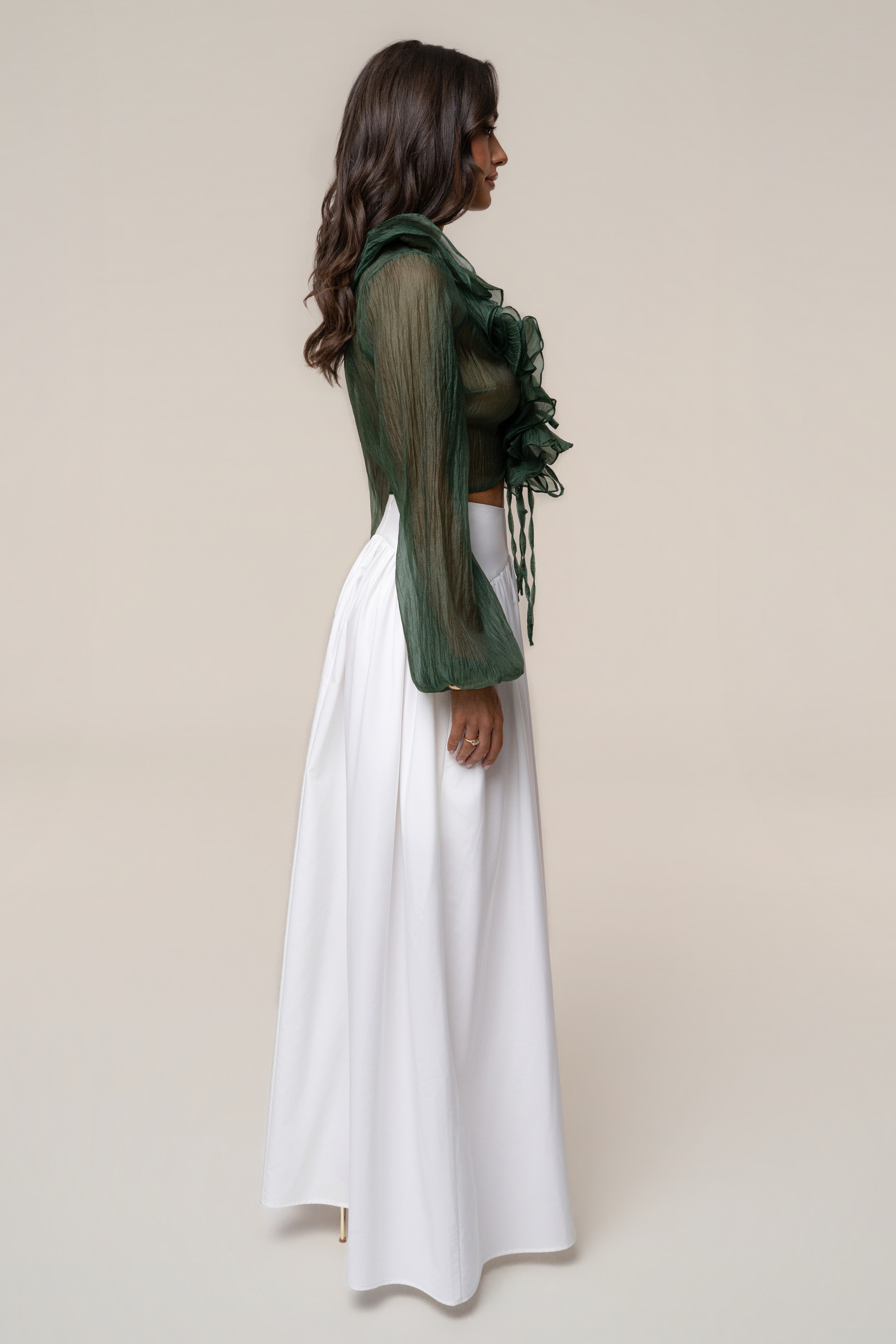 Side profile of a woman wearing a sheer green Delilah Ruffled Top with long sleeves and a white skirt