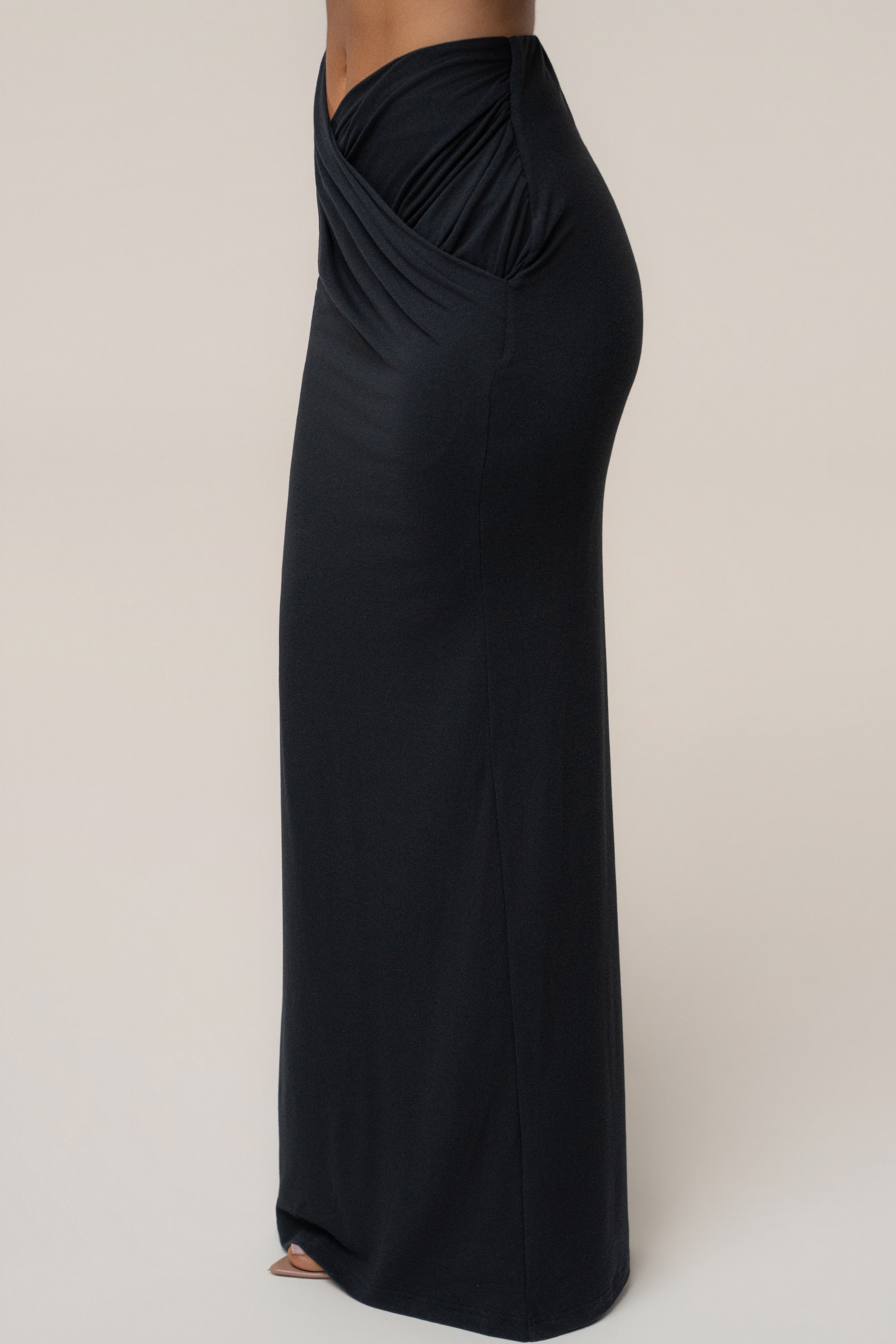 Side view of the model in a black maxi skirt with a ruched draped waist detail