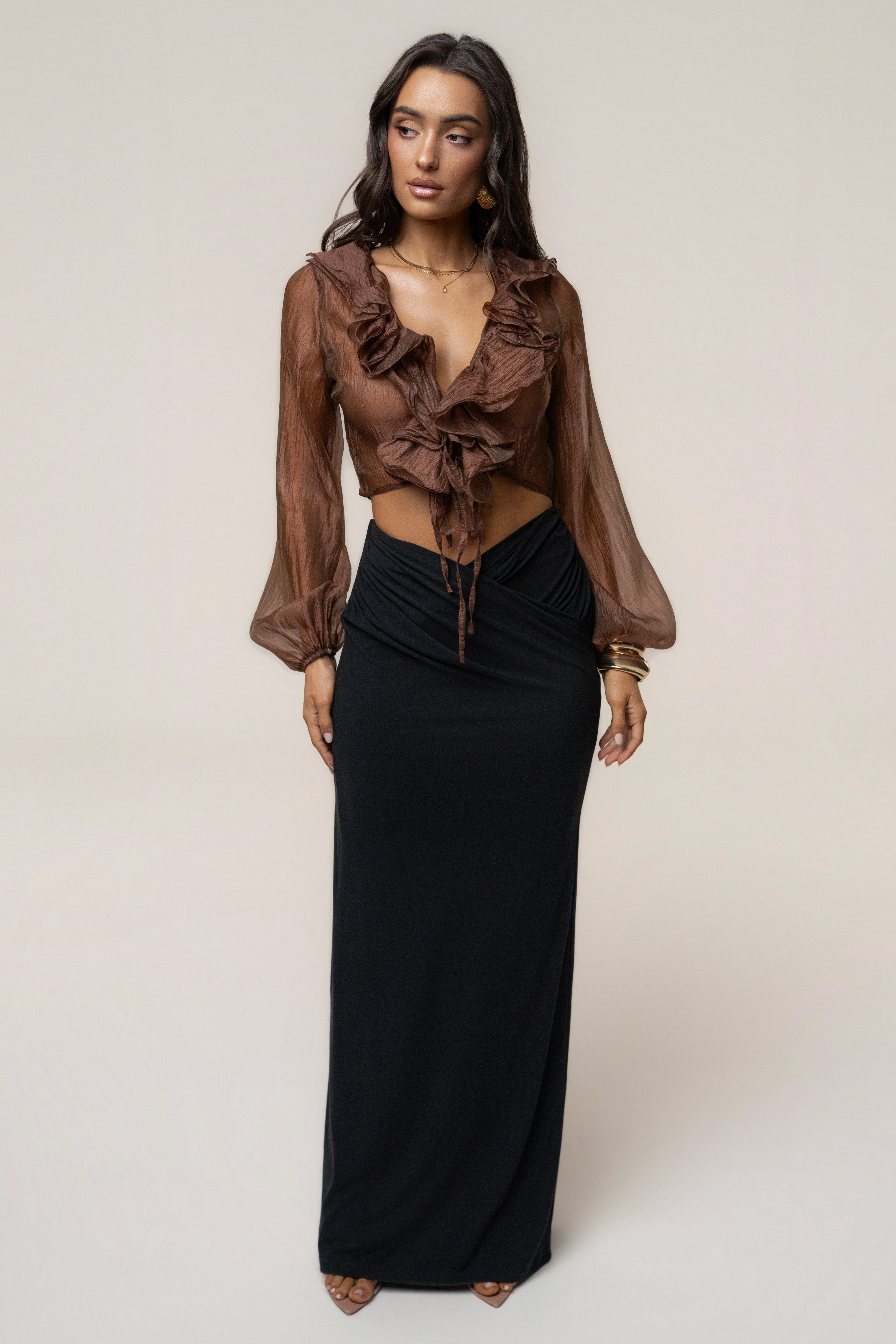 Model wearing a black maxi skirt with a brown sheer ruffled blouse