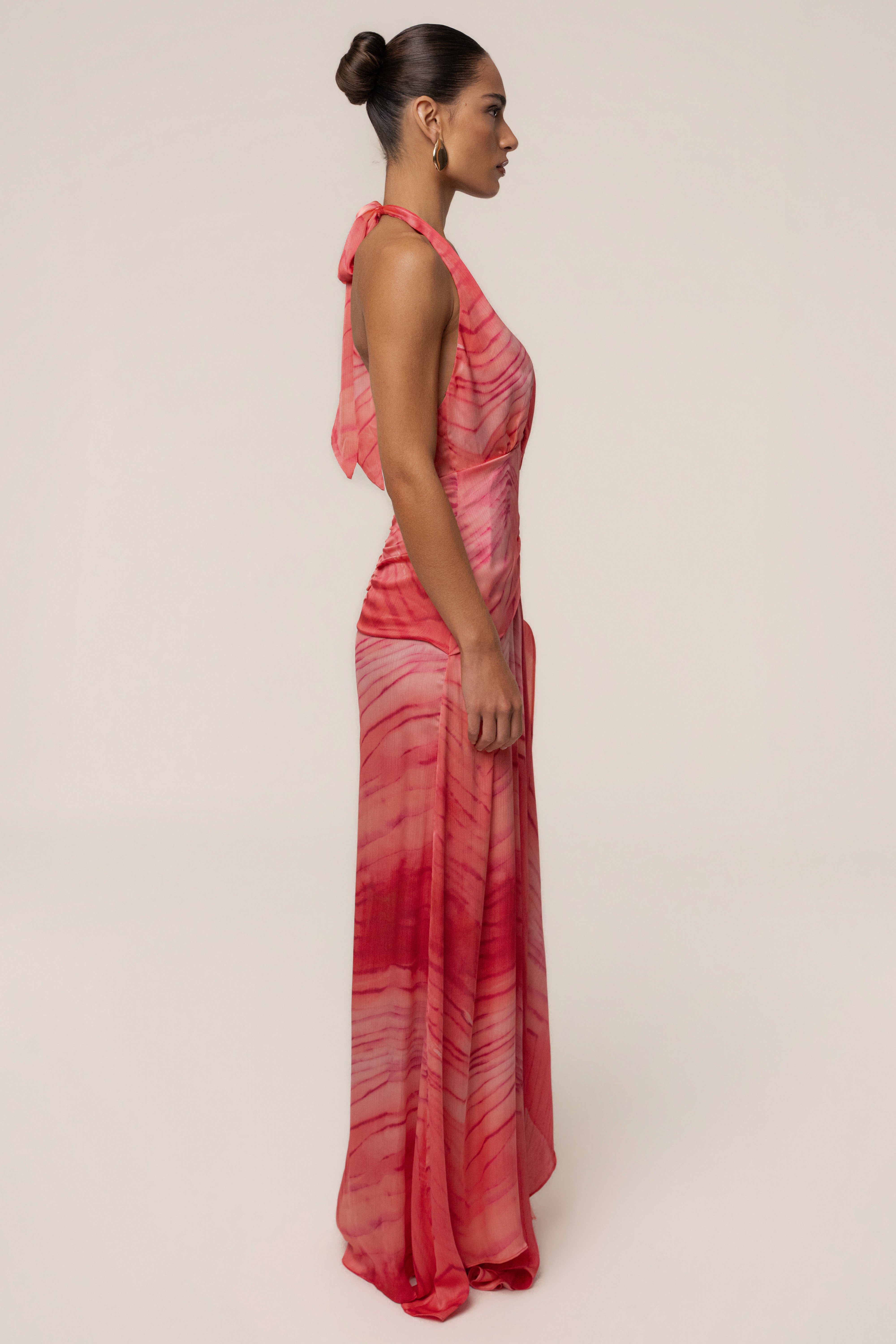 Profile of a model wearing coral red halter back-tie maxi dress with a flowing skirt