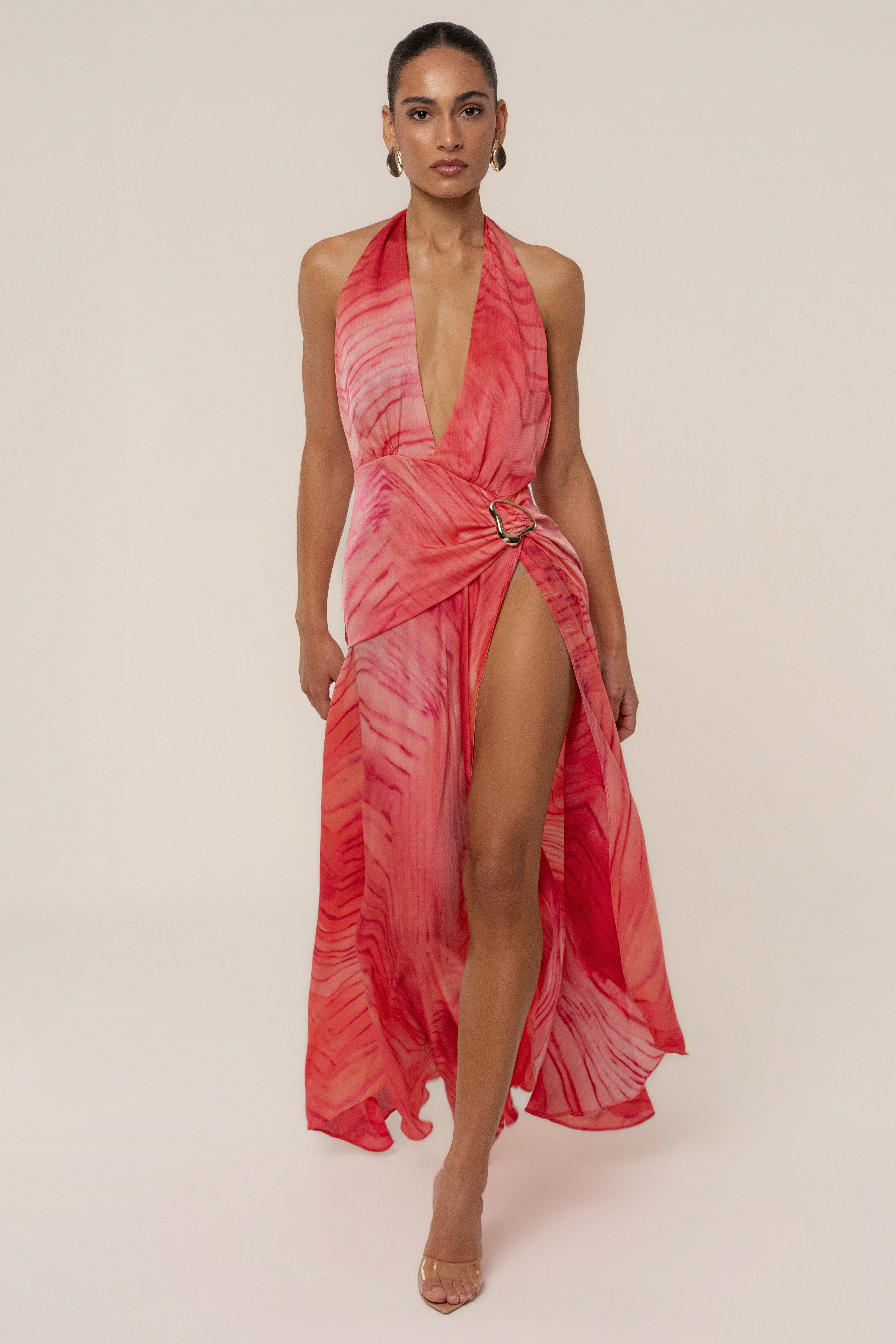 Model wearing coral red Vacation State maxi dress with halter neck deep V neckline, belt with gold buckle and a high slit.