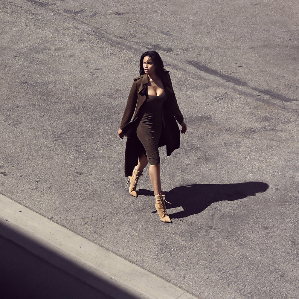 Woman walks on a sunlit urban street in a brown midi dress with a trench coat and tan lace-up boots