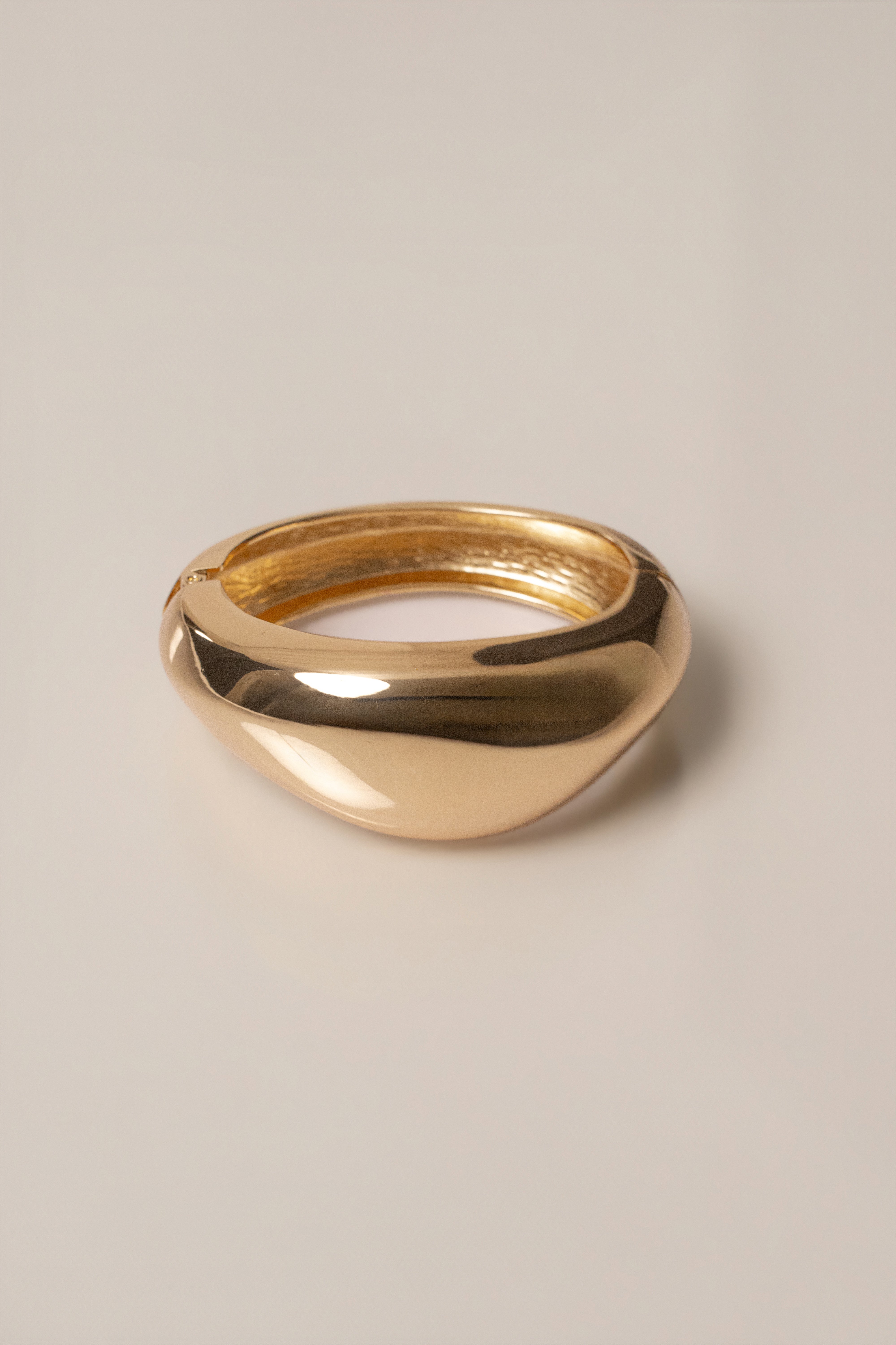 Gold Vittoria hinge bracelet with a smooth rounded band in a close-up shot.