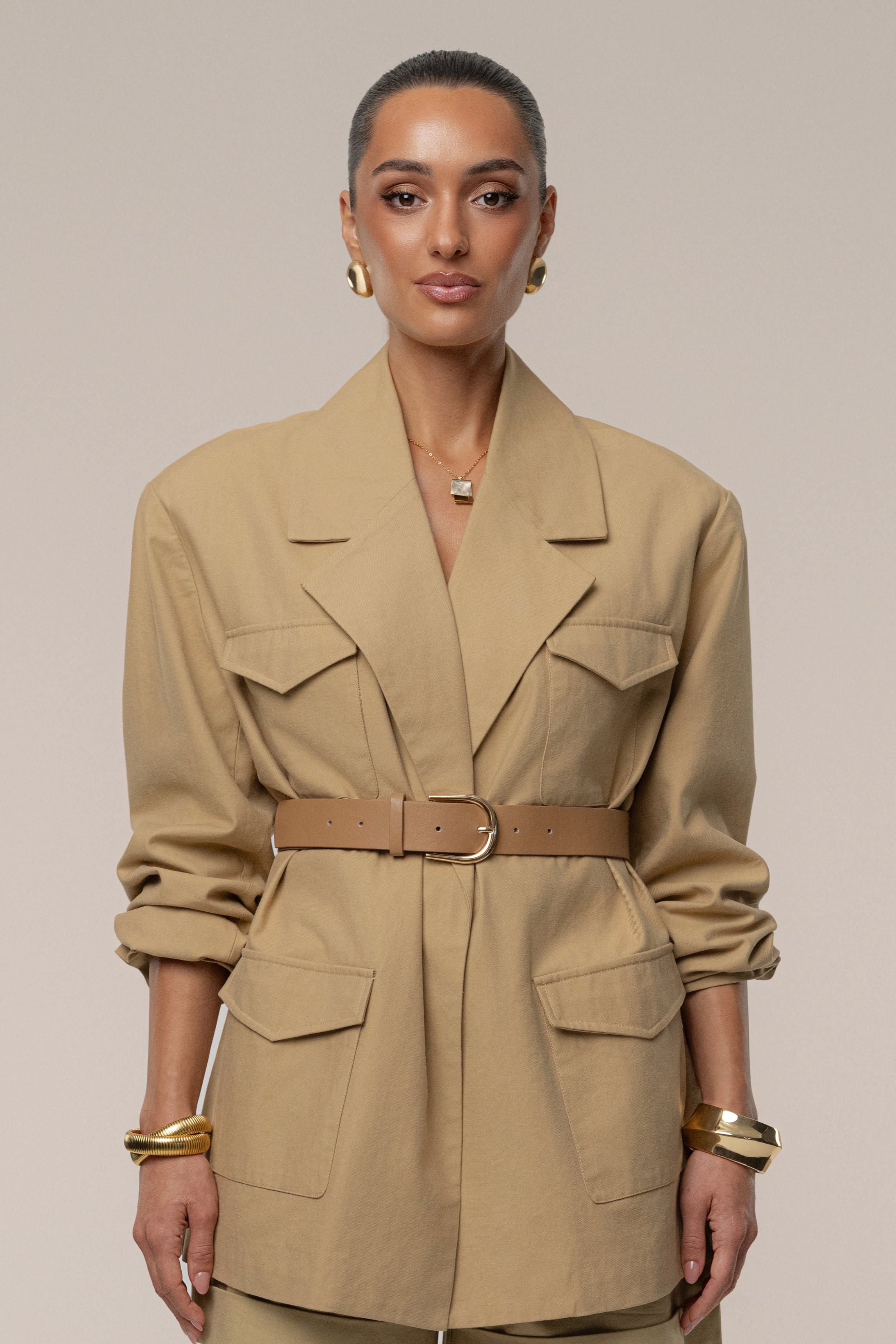 Woman wearing a beige trench coat with a belt on a plain background