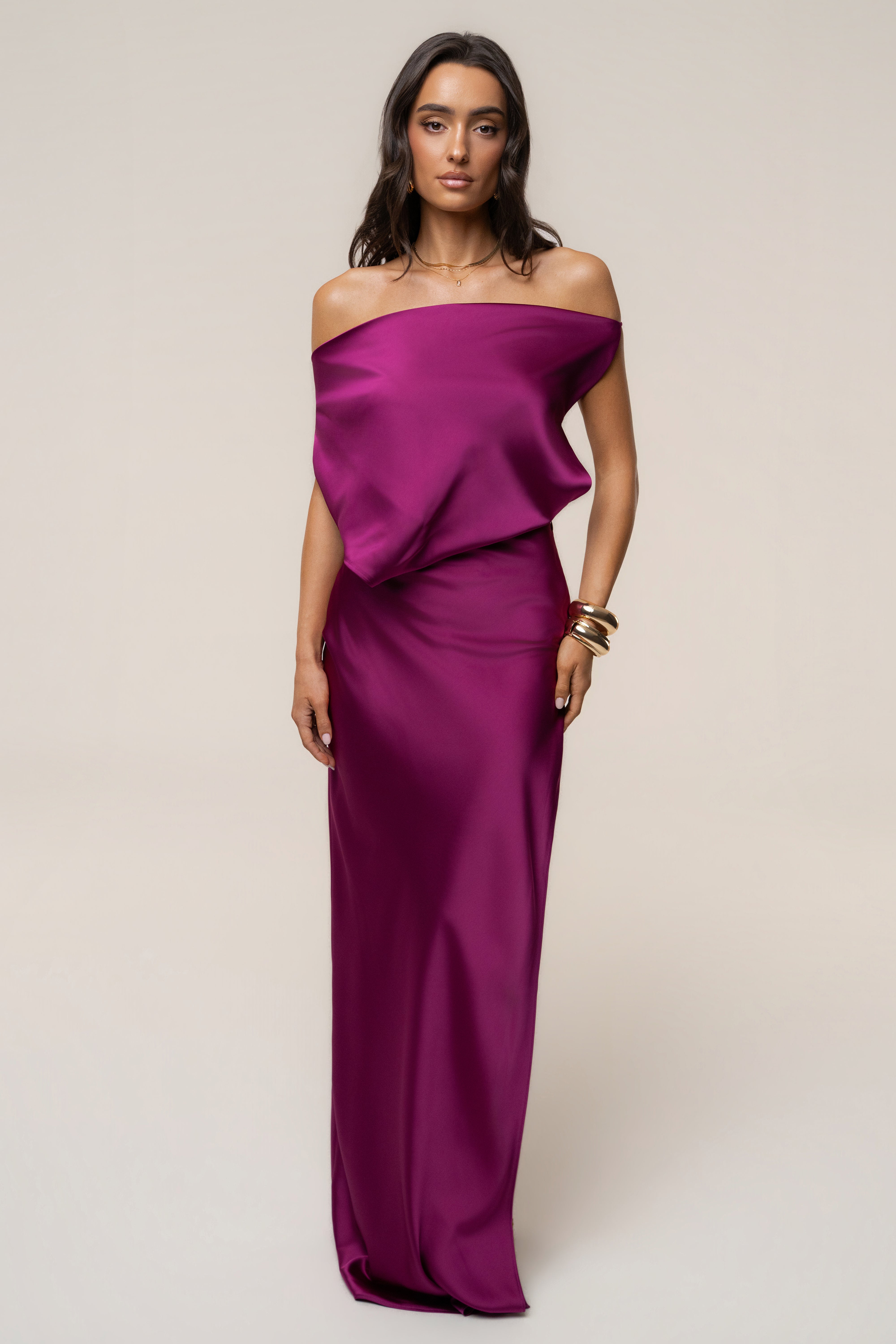 Model wearing a fuchsia Delmara Cowl Maxi Dress with an off the shoulder draped neckline and gold bracelets