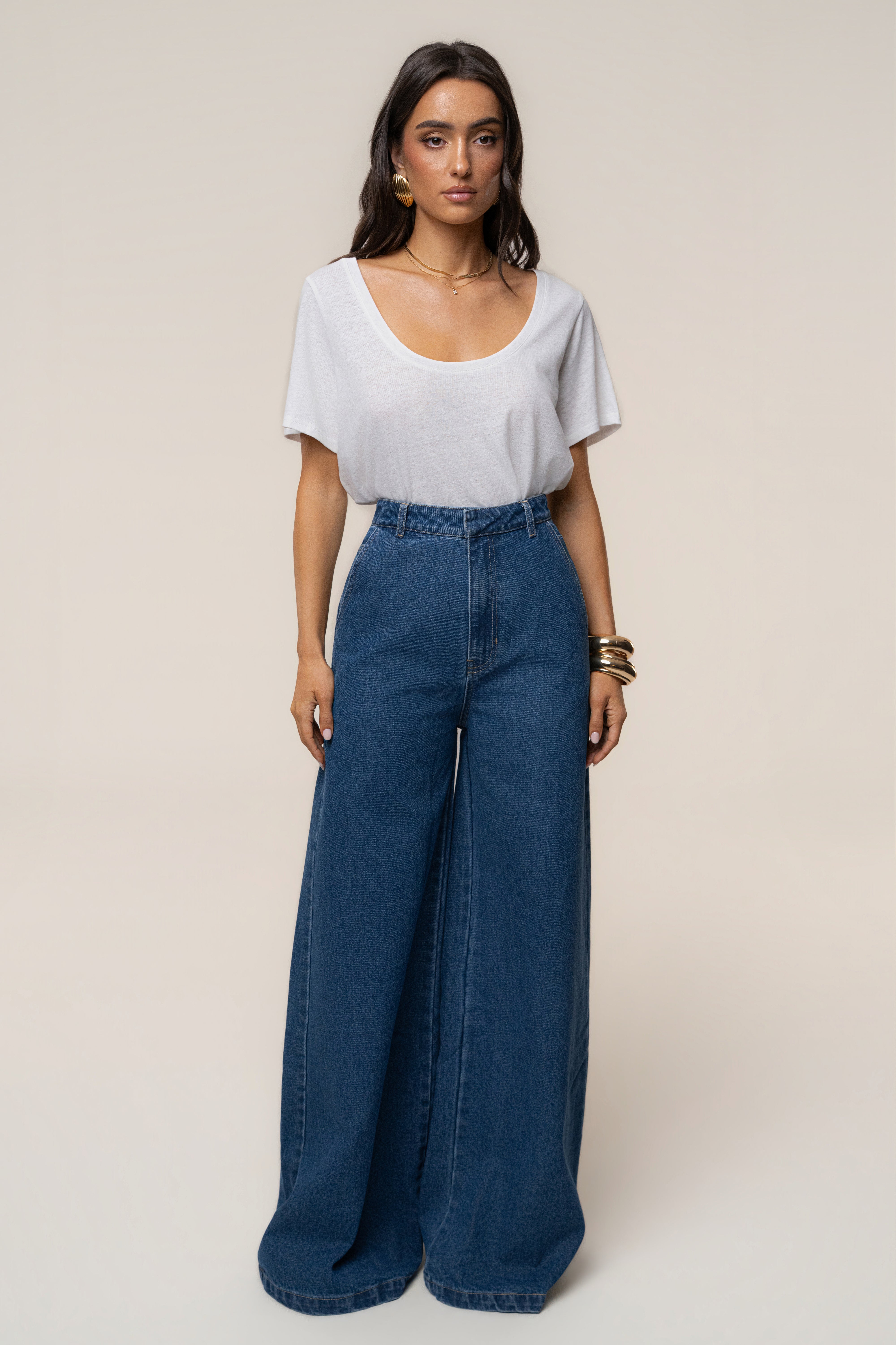 Full-length view of a model wearing medium wash wide-leg denim jeans with a white top against a beige backdrop