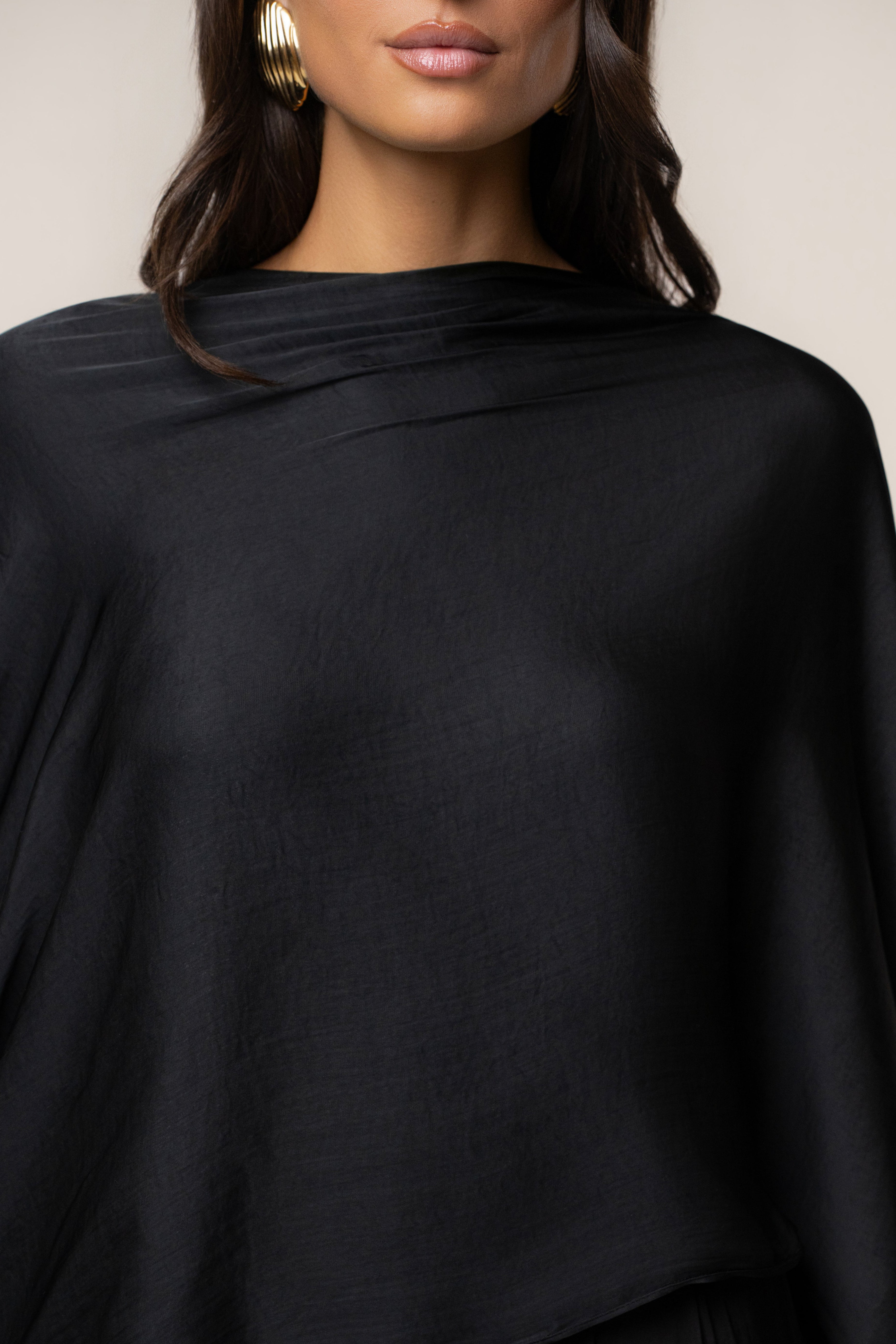 Close up of a woman wearing a black draped off the shoulder top with a gold hoop earring.