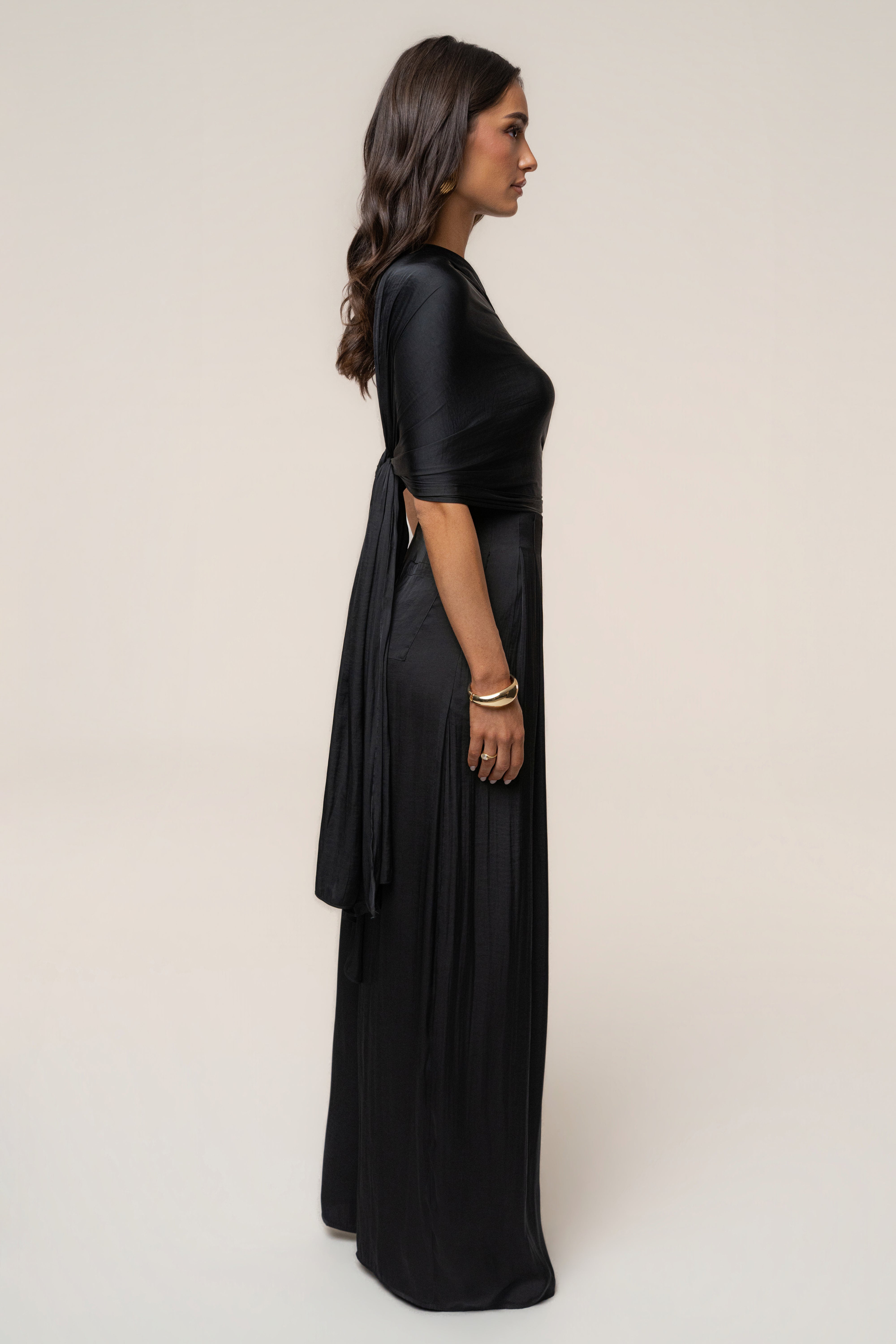 Side profile of a model wearing the Black Marina Multi-Wrap Scarf tied at the back over a black dress