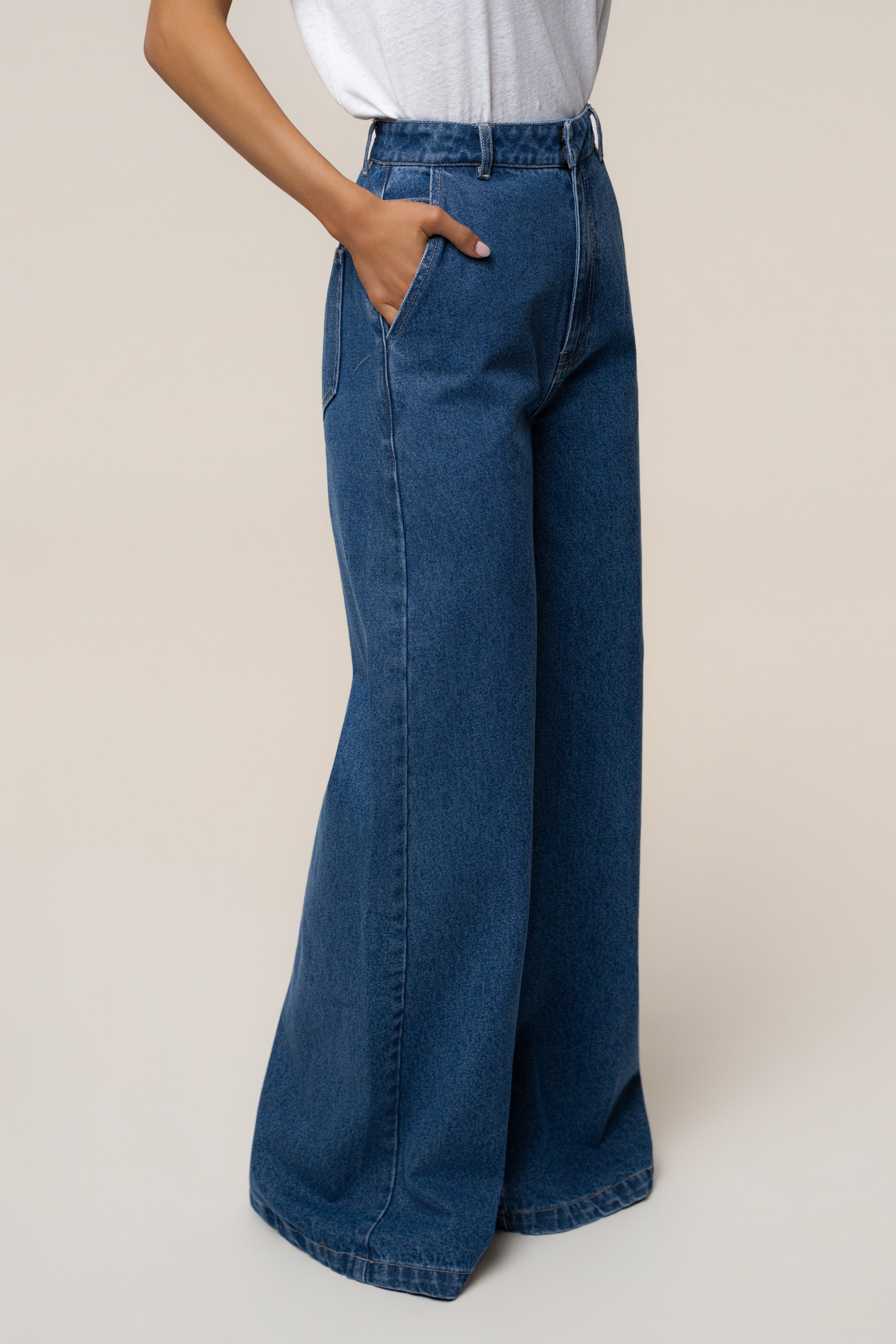 Model wearing medium wash wide leg denim jeans with hand in front pocket and white top.