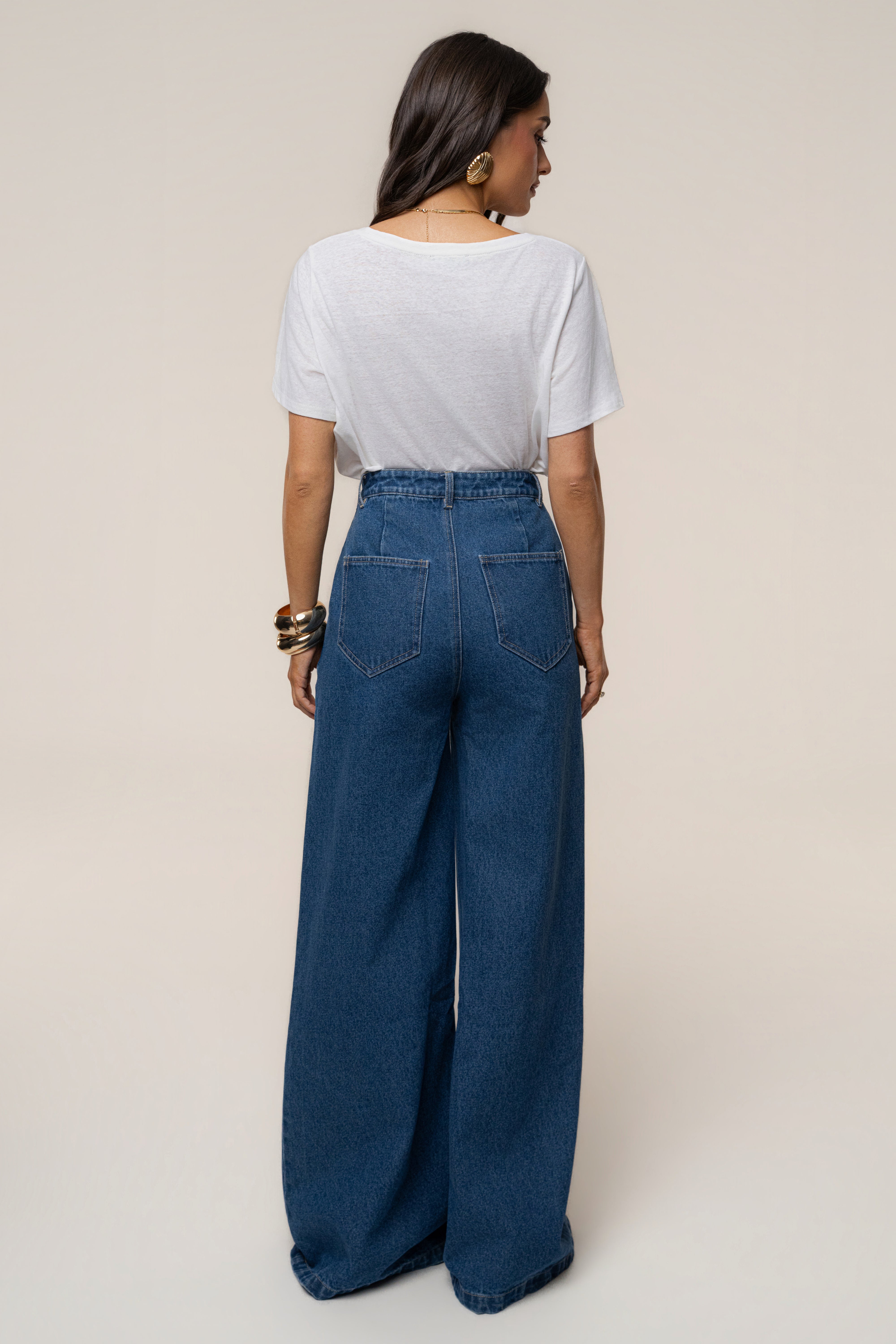 Back view of a woman wearing a white short sleeve tee tucked into medium wash wide leg denim jeans with back pockets.