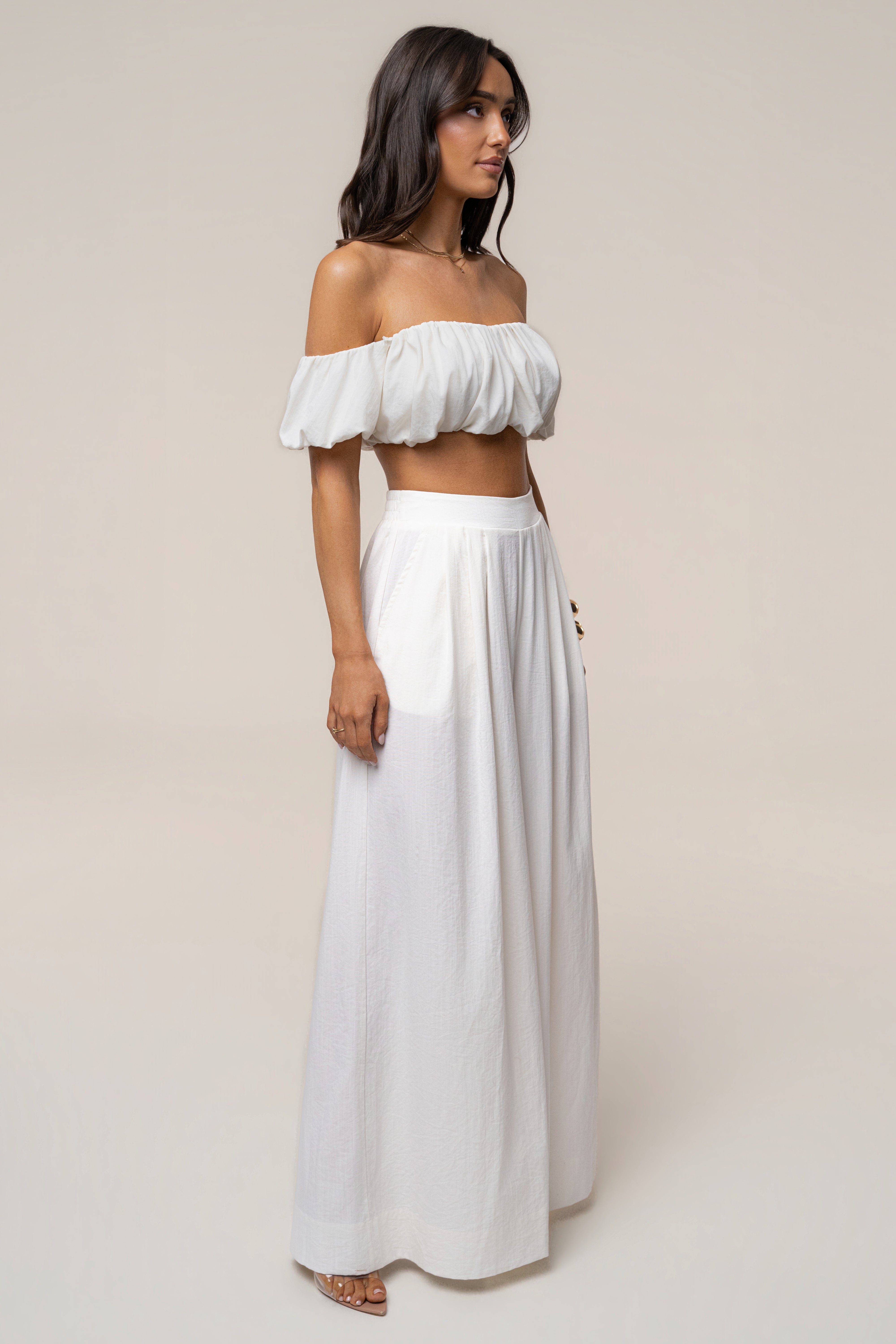 Profile view of a model wearing ivory Sunset Breeze pant set with an off-shoulder crop top and wide-leg pants.