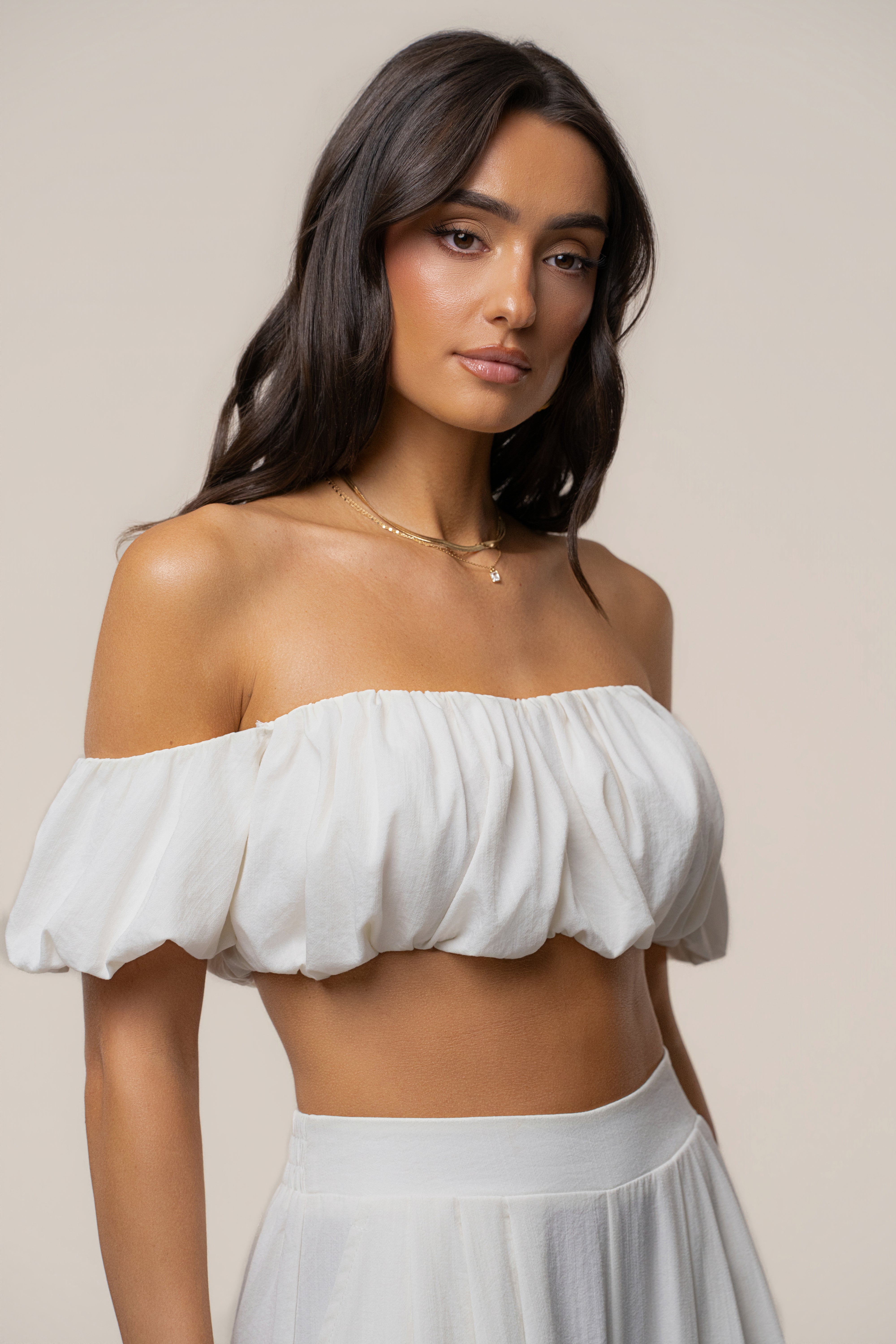 Ivory Sunset Breeze off the shoulder top worn by a model with a delicate gold necklace