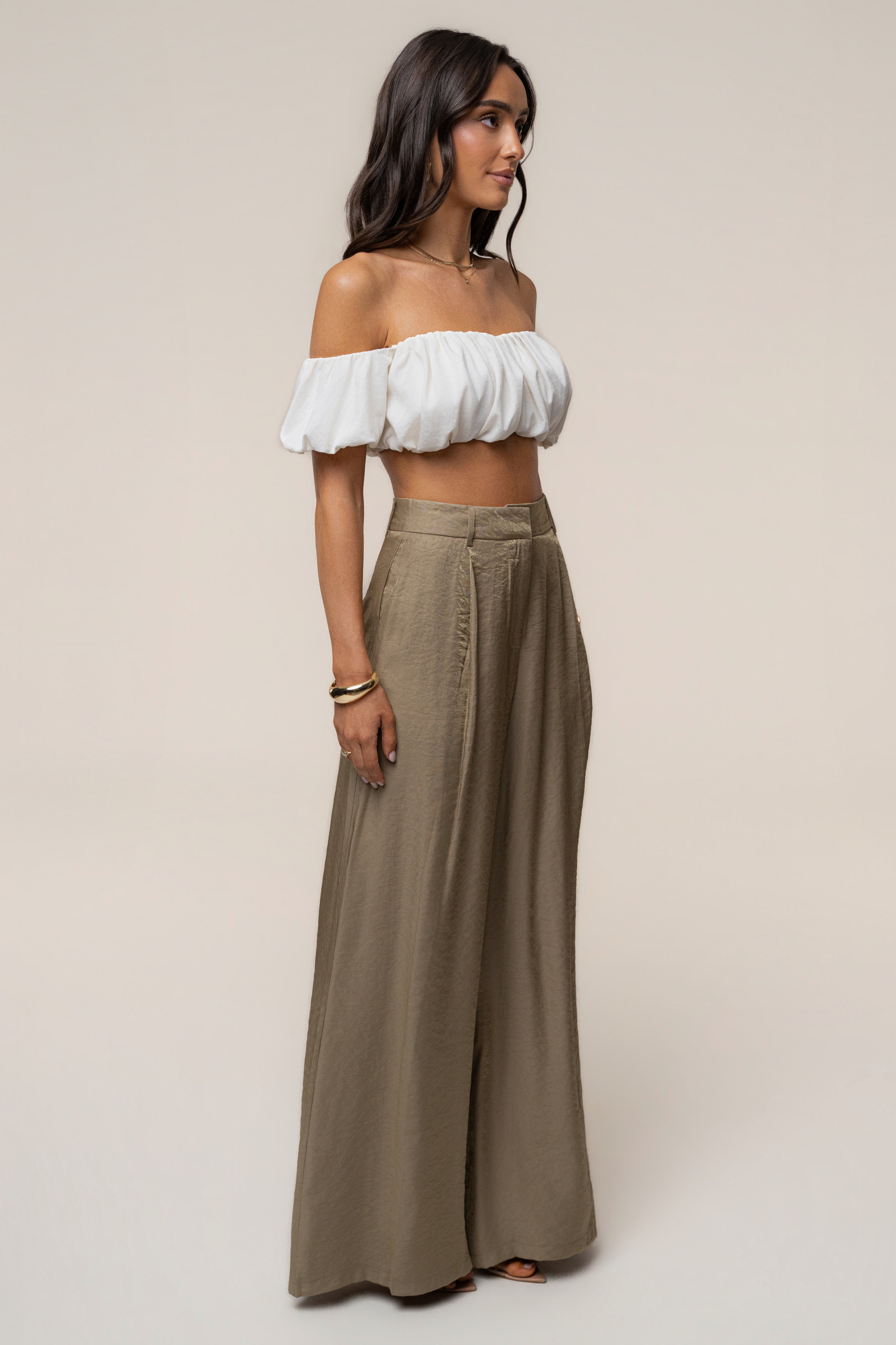 Side profile of a model wearing an off the shoulder white top with olive Monaco wide leg pants.