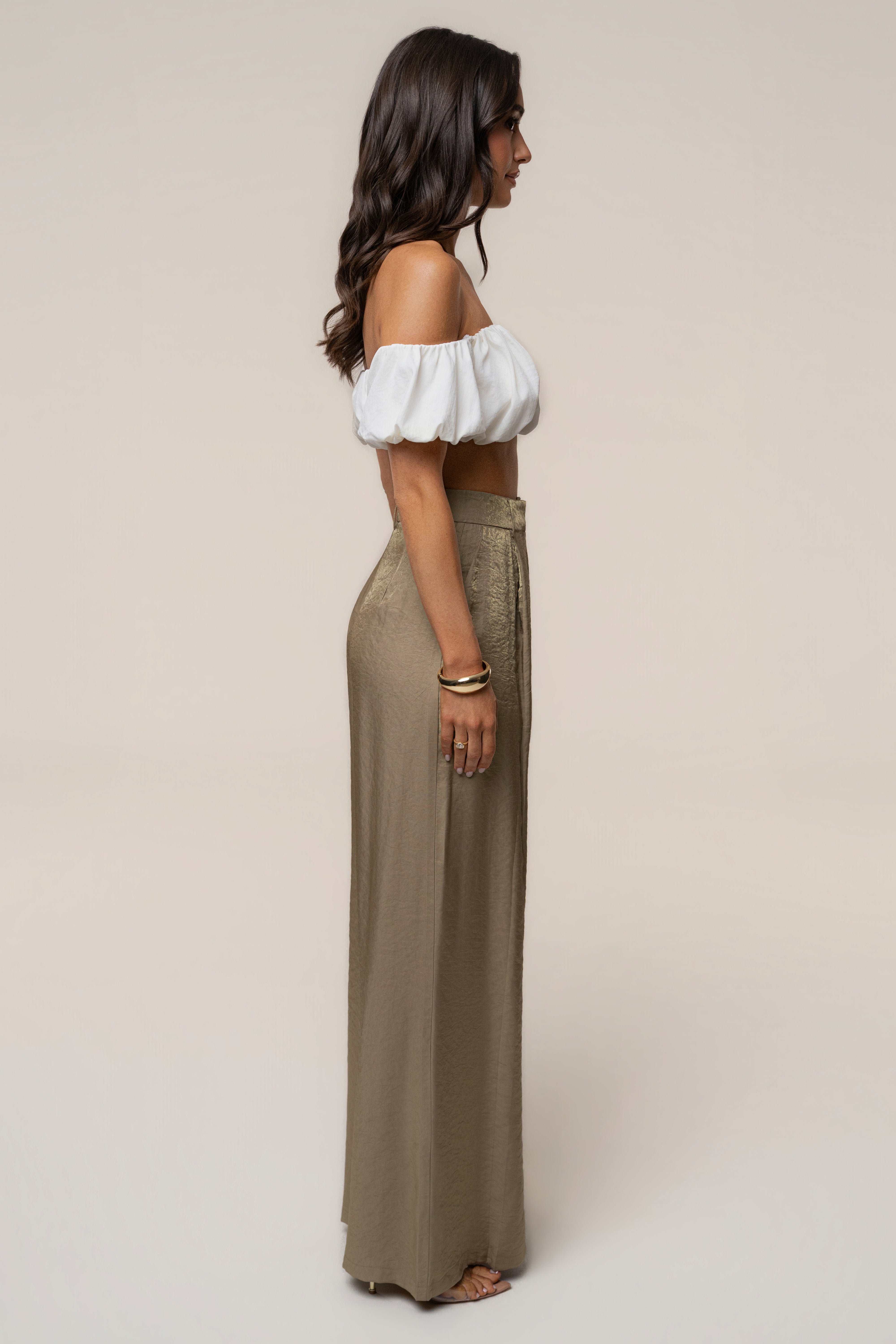 Side profile of a model wearing a white off the shoulder top and olive wide leg pants.