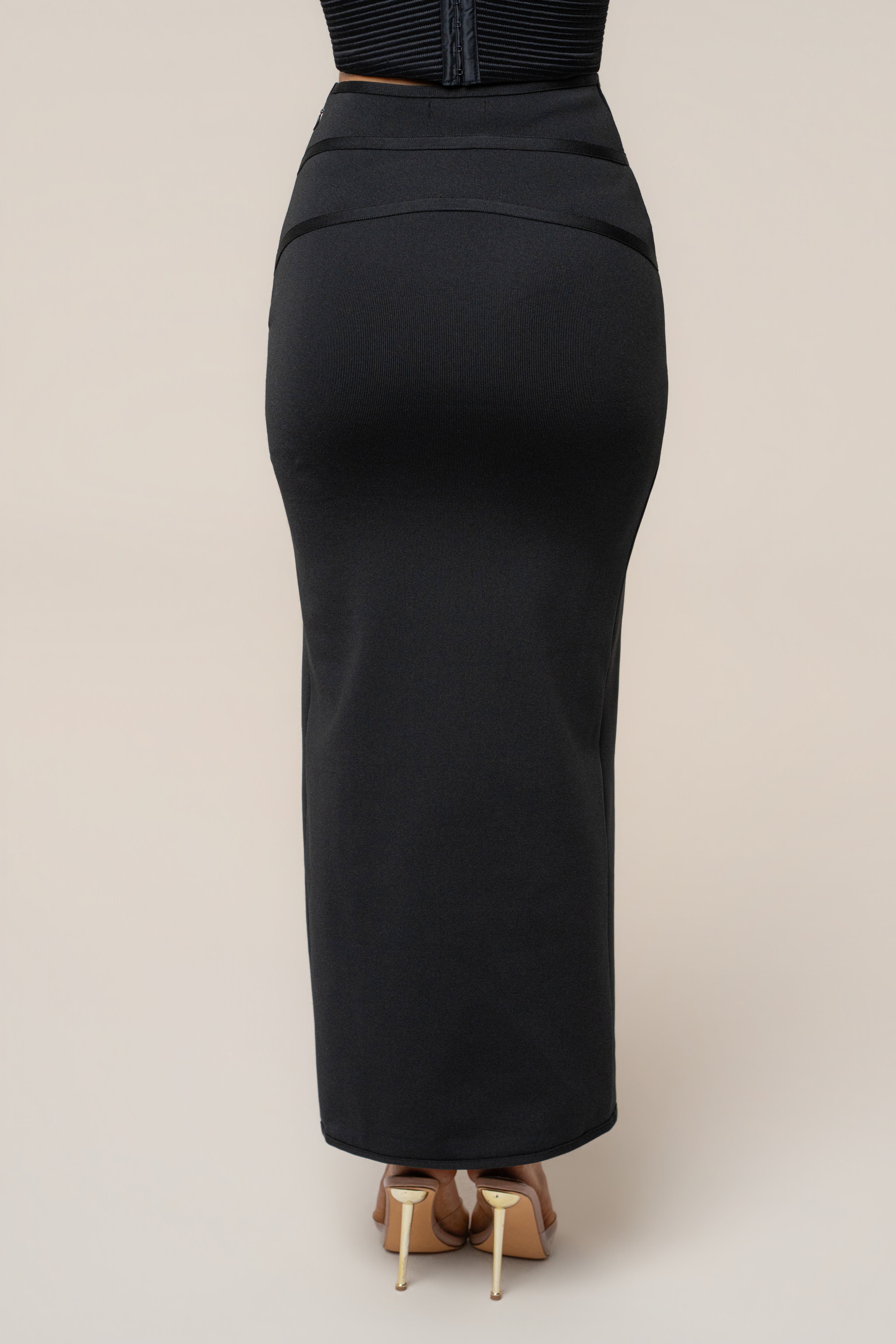 Back view of the black essential form maxi skirt showing a center back zipper and panel details.