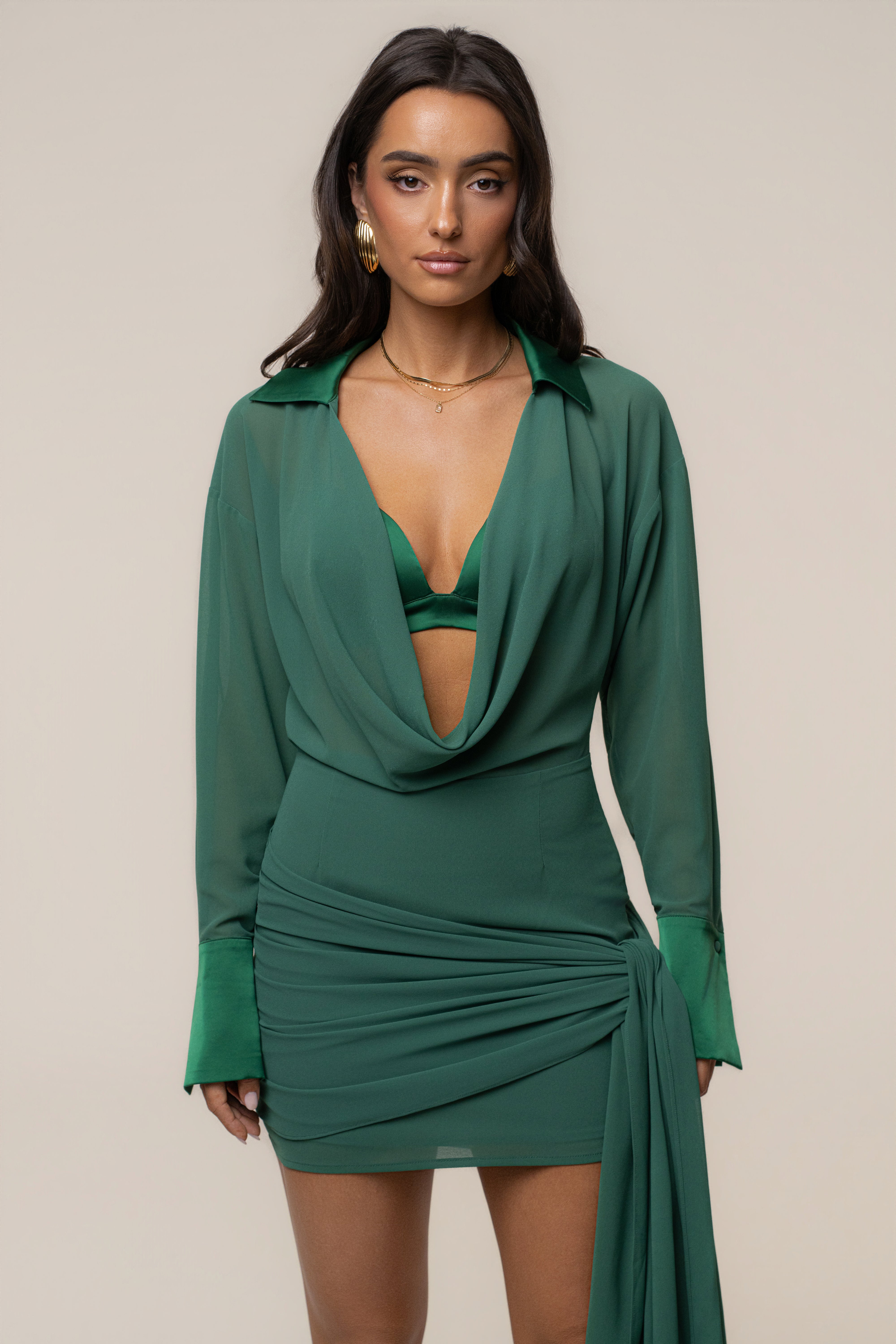 Model wearing a green draped wrap mini dress with a plunging neckline and long sleeves against a neutral backdrop.