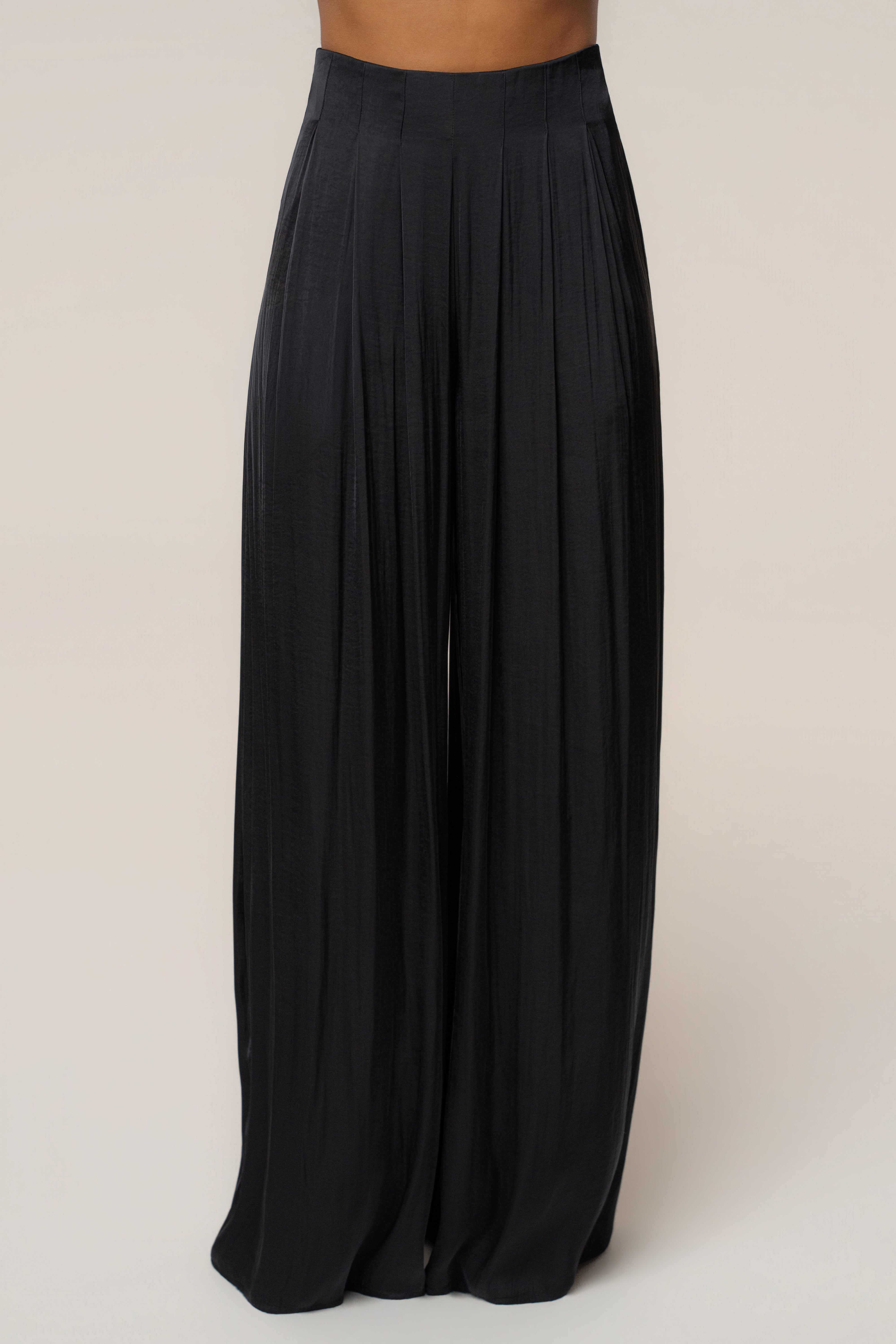 Close up of black pleated trouser waist showing tailored waistband and front pleats.