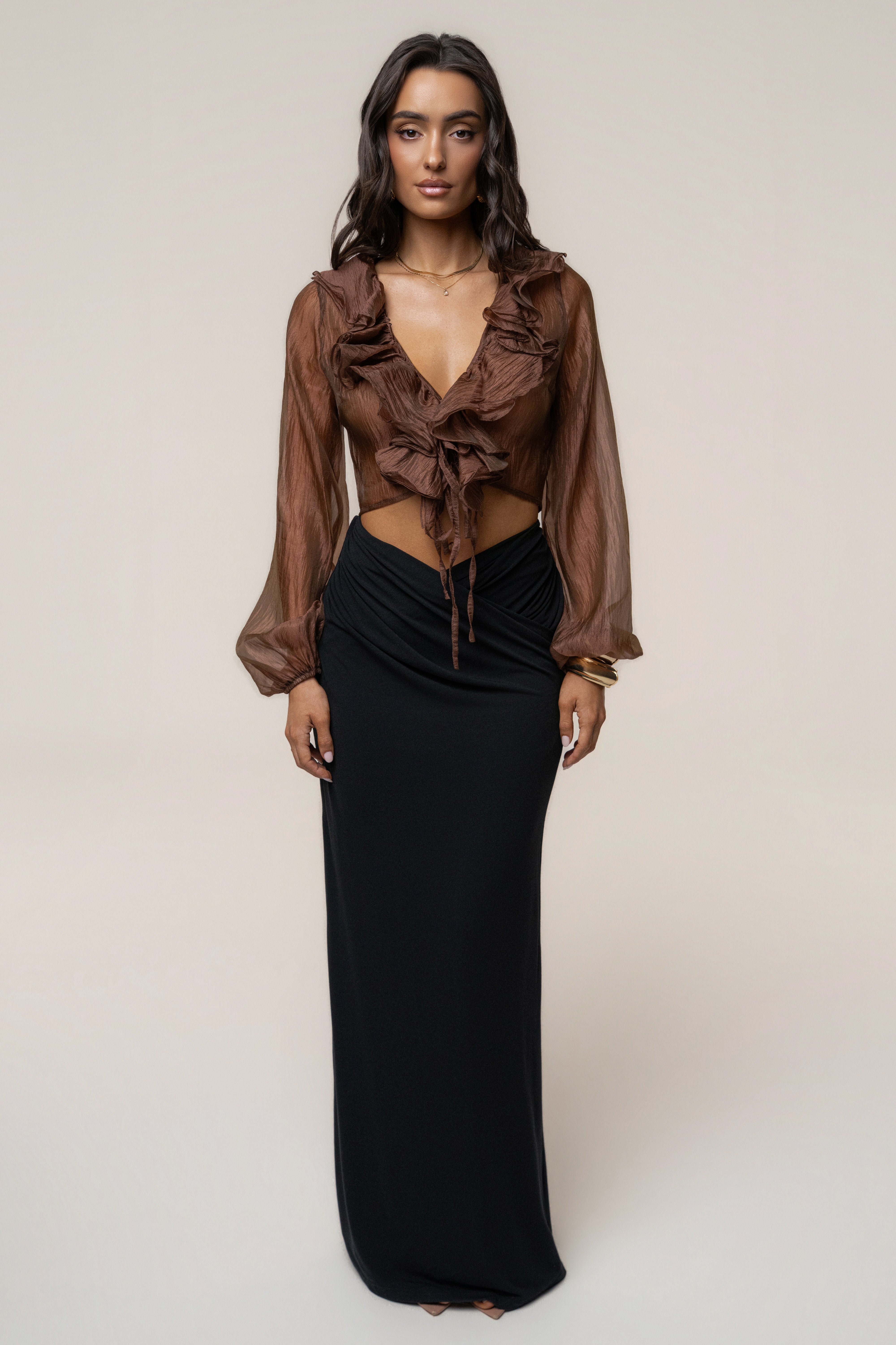 Front view of a model wearing a brown sheer ruffled blouse with a black maxi skirt.