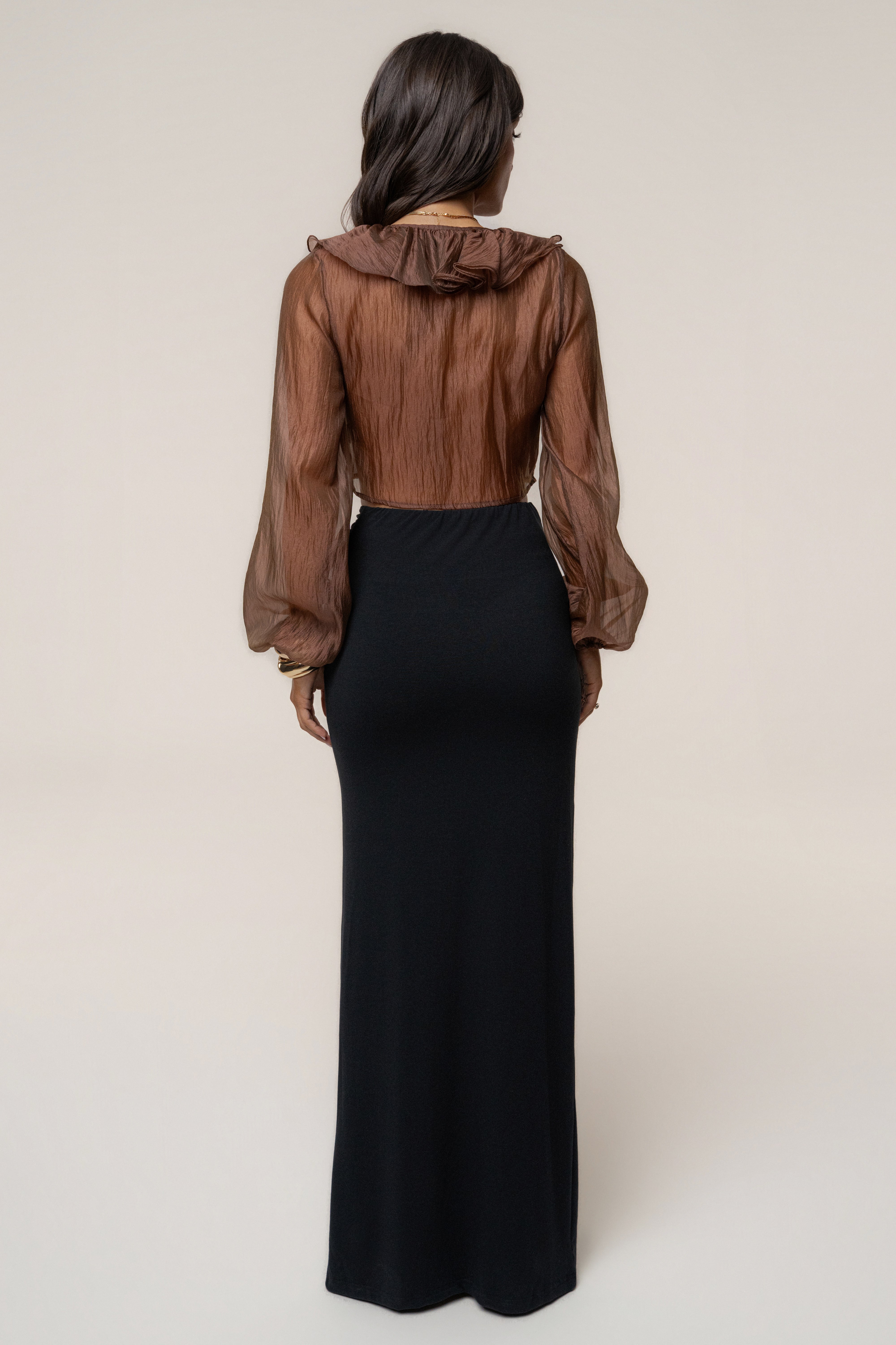 Back view of a model wearing a brown sheer blouse paired with Black Passion Maxi Skirt