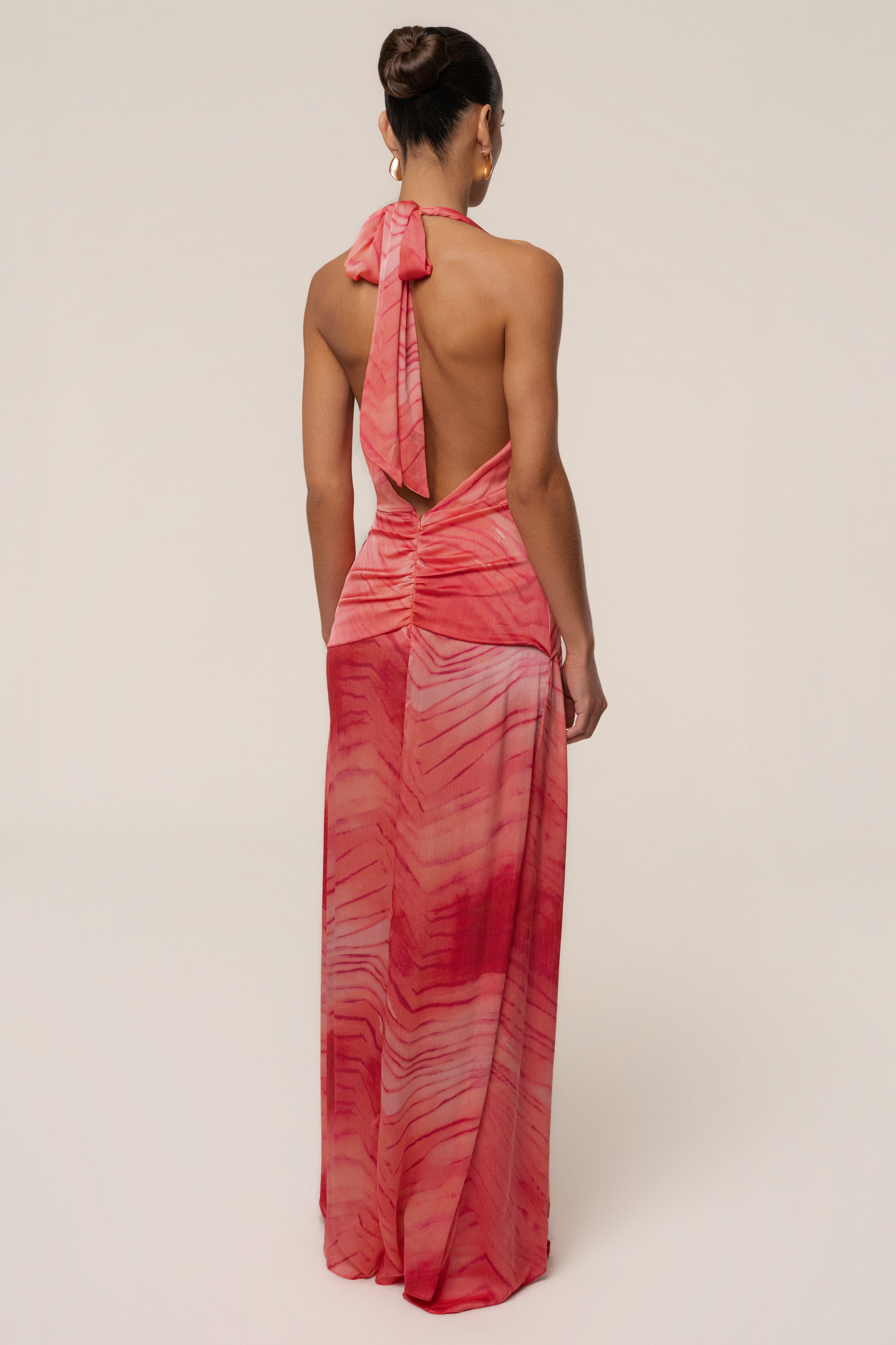 Back view of a model wearing coral red tie-dye Vacation State maxi dress with halter neck and open back.