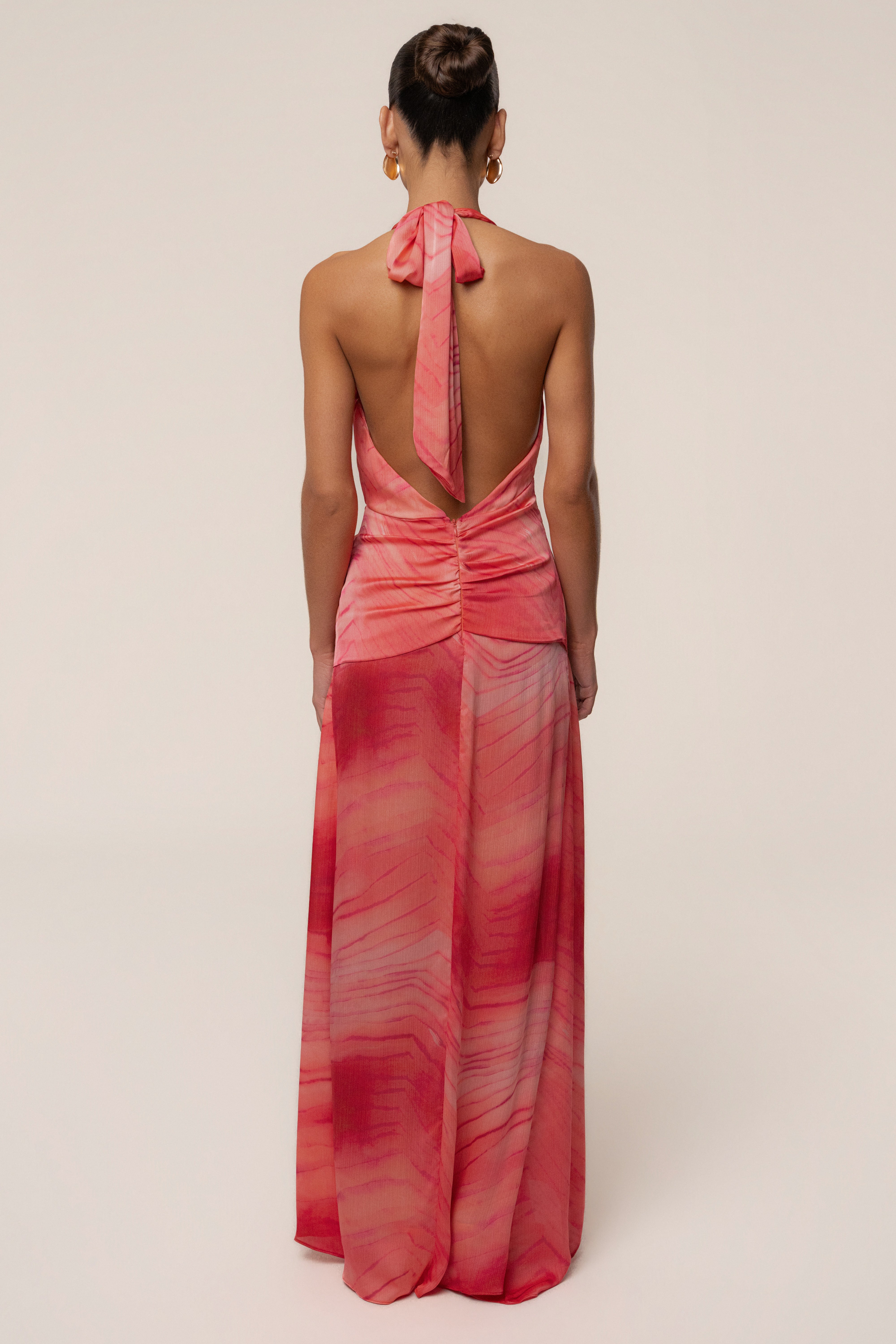 Back view of a model wearing coral red tie-dye maxi dress with an open back and halter neck