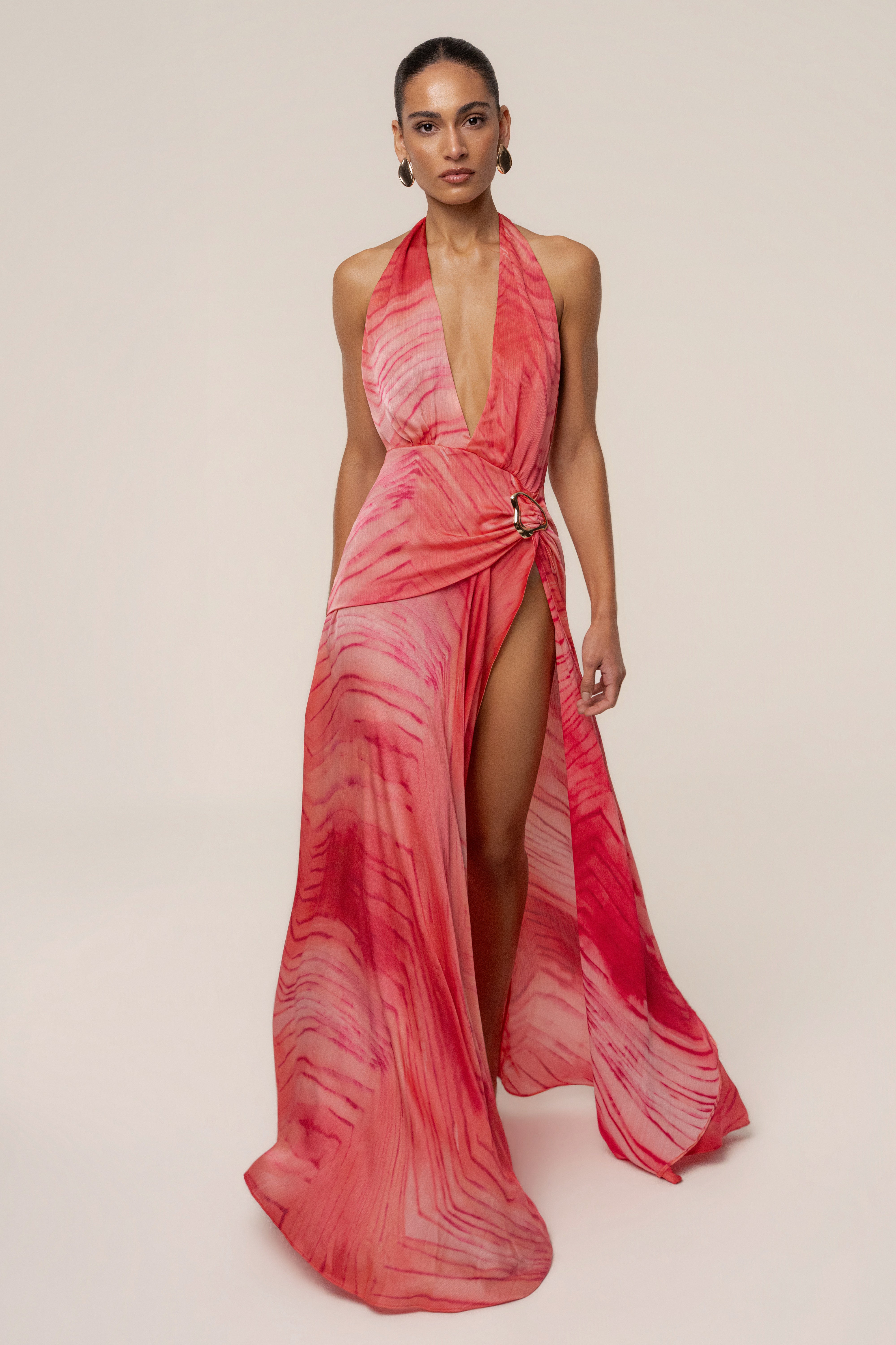 Portrait view of coral red halter neck maxi dress with waist wrap and high slit.
