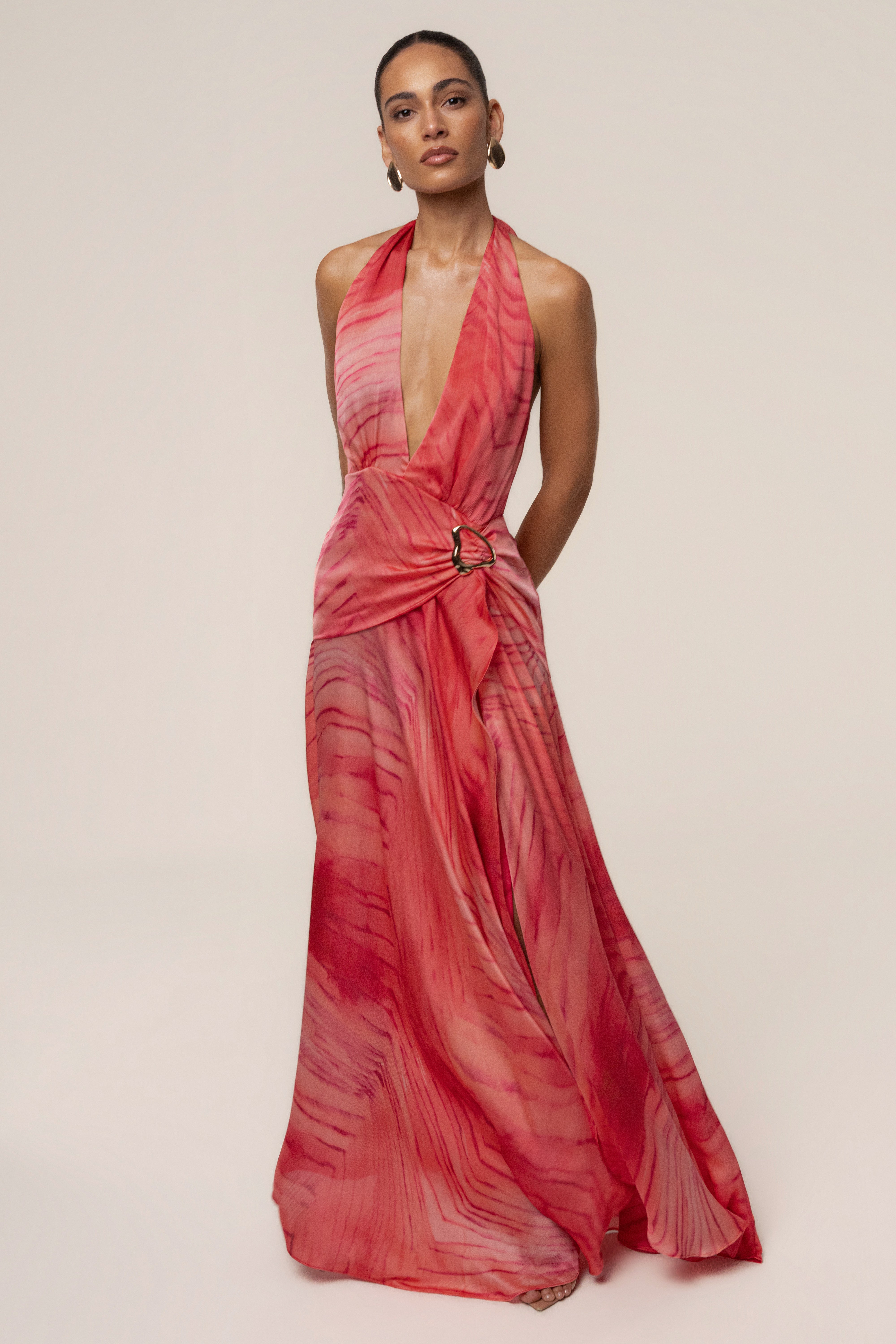 Model wearing coral red Vacation State Maxi Dress with halter neckline and deep plunging front, belt with ring at the waist.