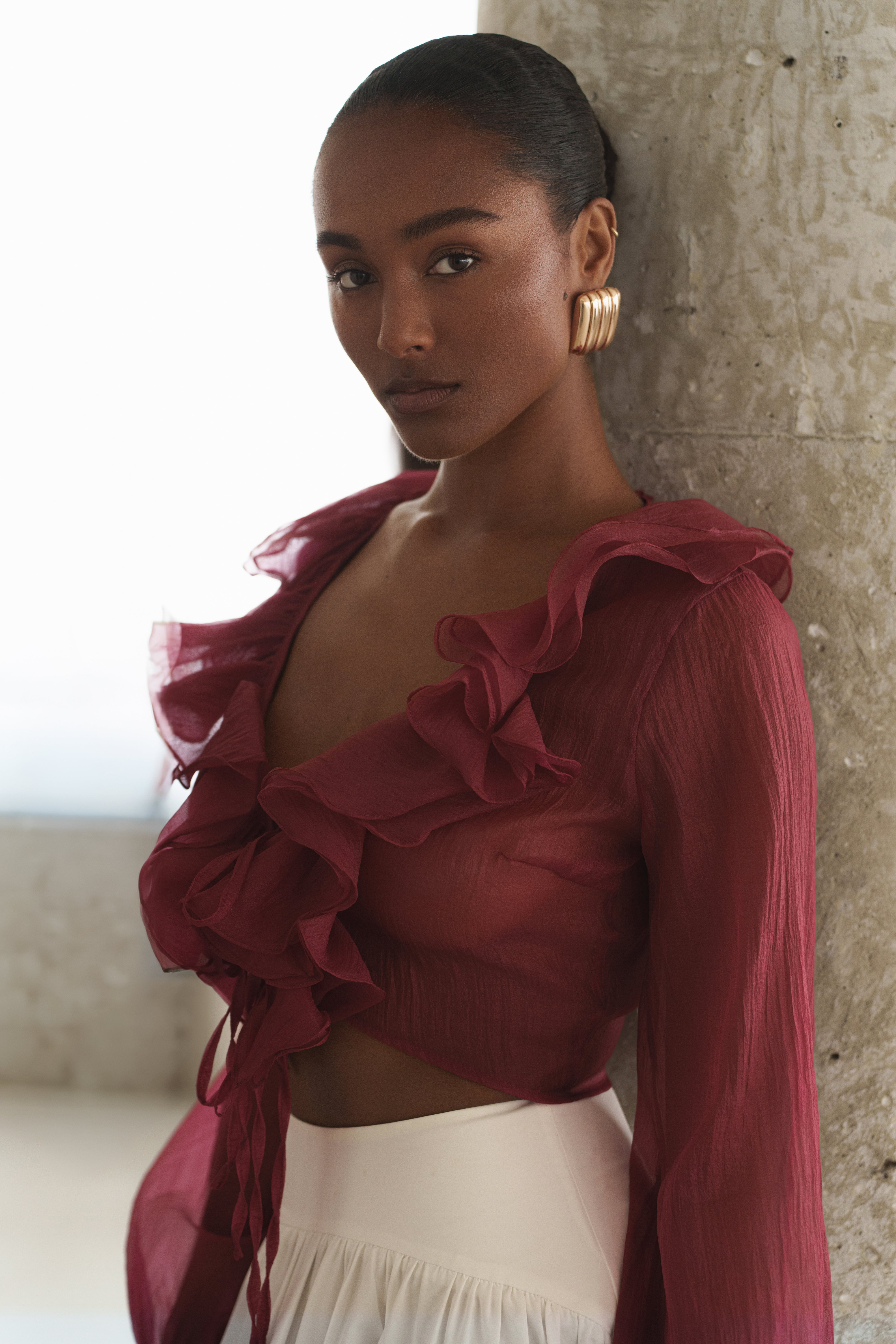 Model wearing berry Delilah ruffled top with bold ruffles against a textured wall